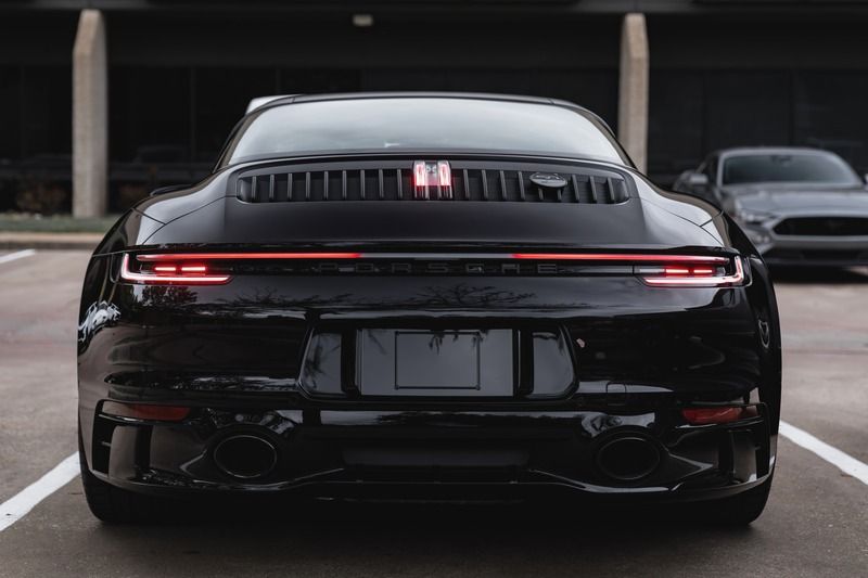 Rear view of a black sports sedan parked in a garage, with a full-width red taillight strip.