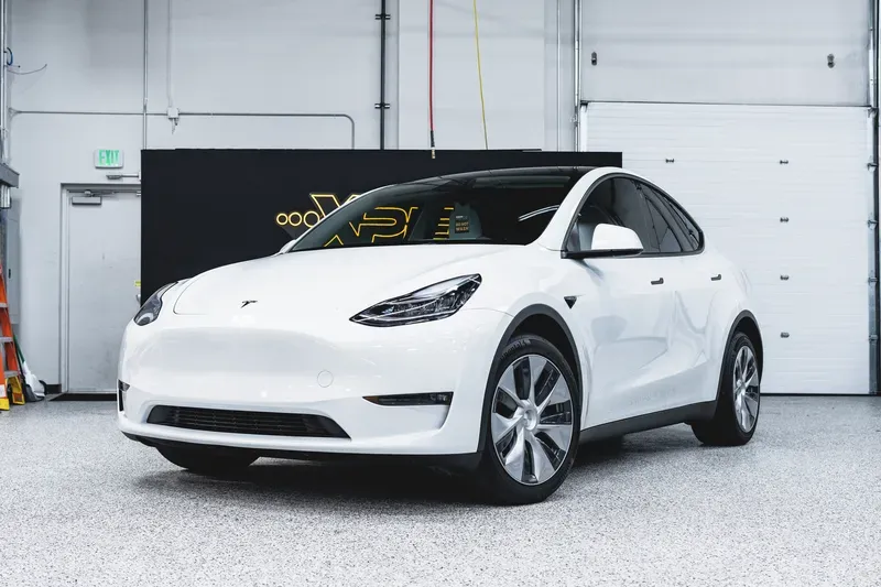 White Tesla Model Y parked indoors in a bright garage, front three-quarter view
