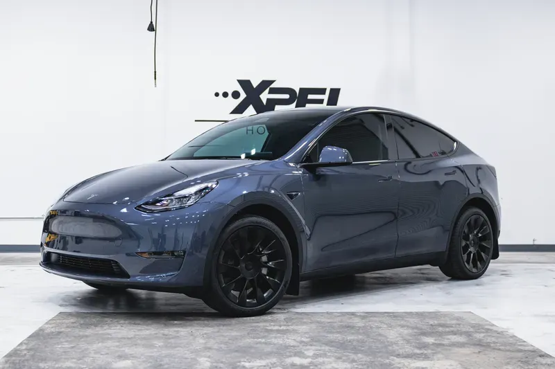 Dark blue Tesla Model Y in a studio with XPEL signage, shown in front three-quarter view