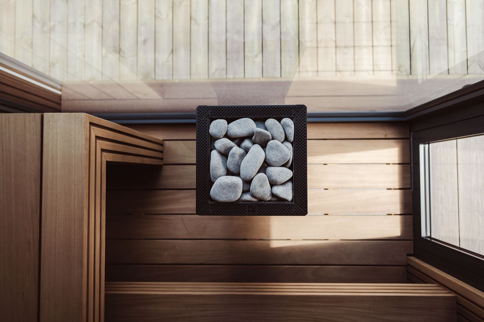 Overhead view of a small square tray filled with gray stones on a wooden floor beside windows