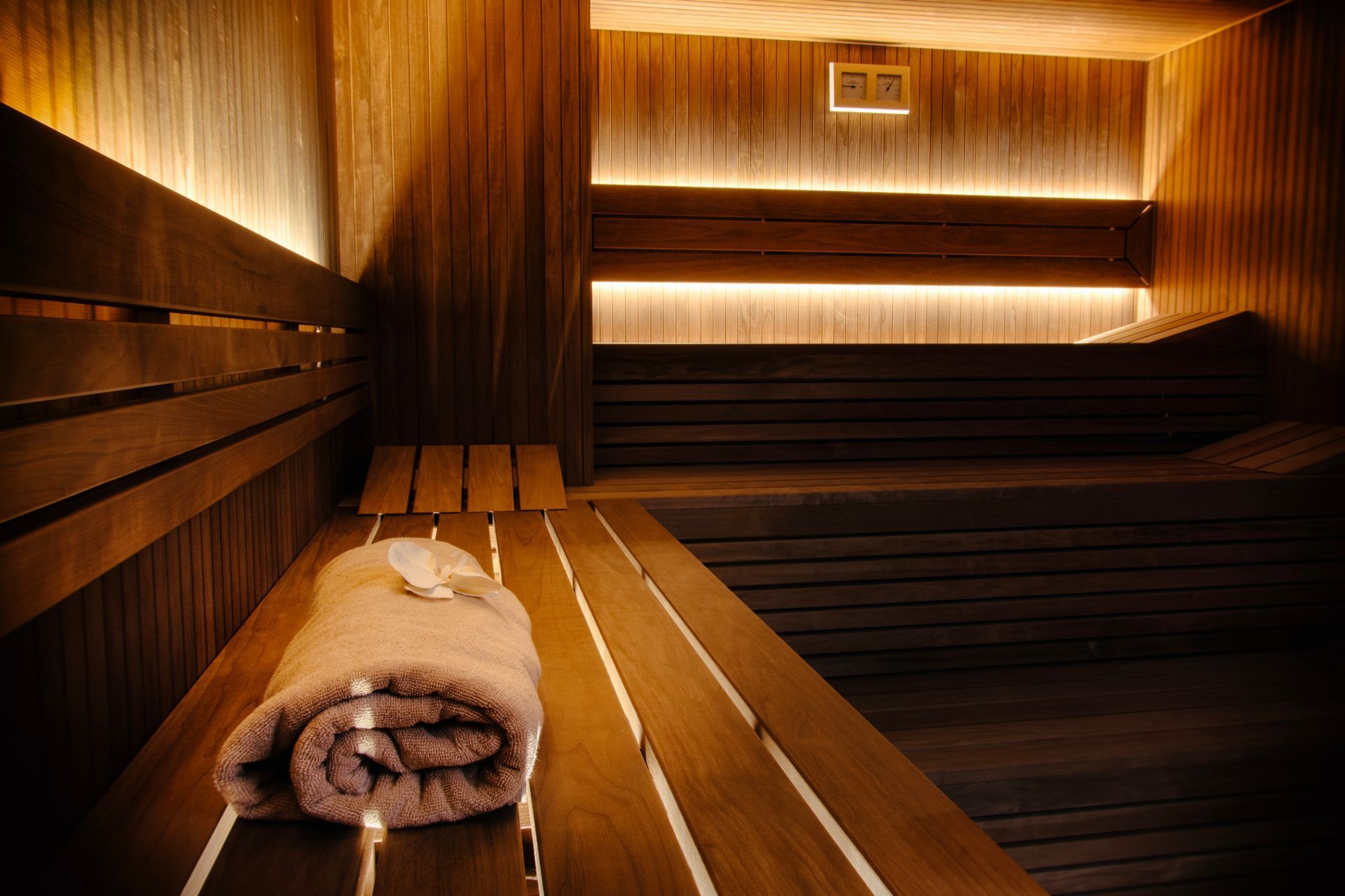 Wooden sauna with bench seating, warm lighting, and rolled towels in the foreground