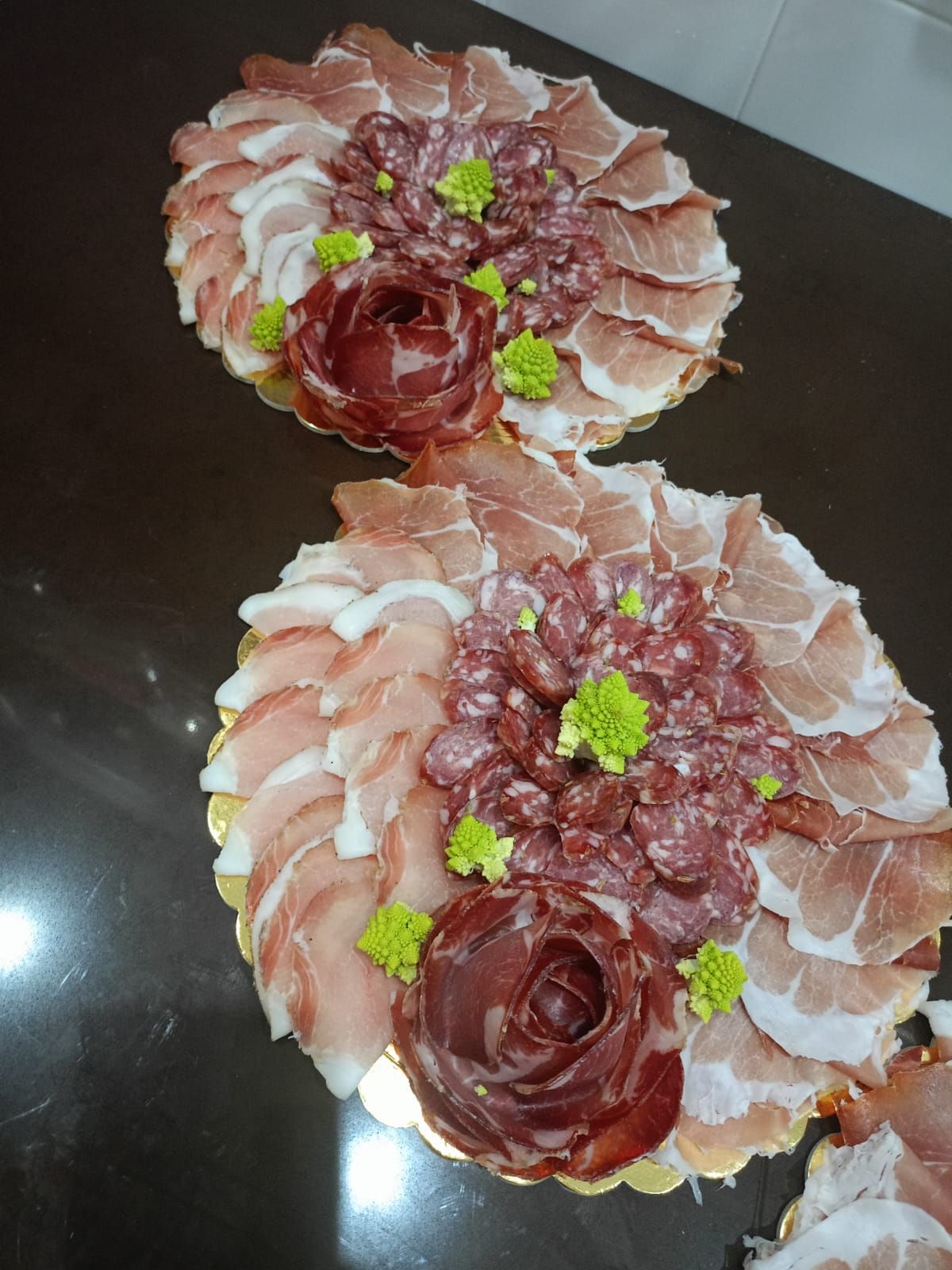 Due vassoi di cibo floreali con affettati disposti a formare rose su un tavolo scuro