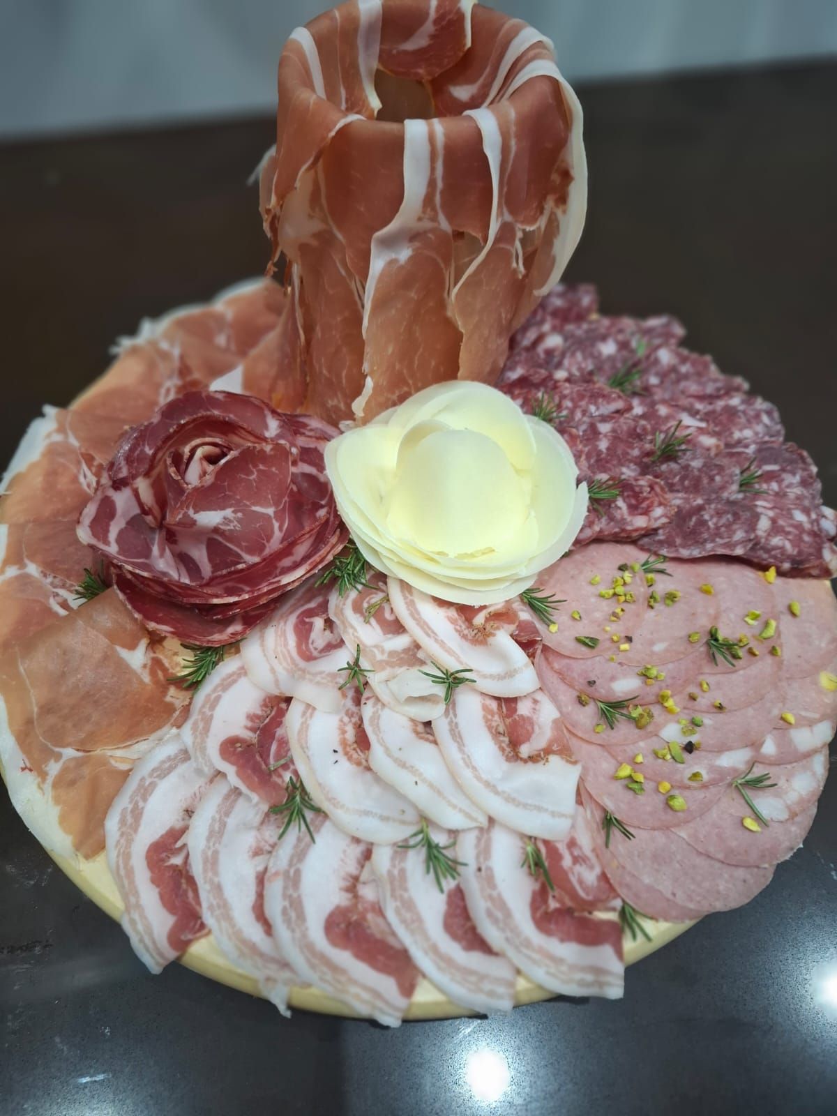 Tagliere di salumi con prosciutto crudo piegato, rosette di salame, formaggio e guarnizioni su un piatto
