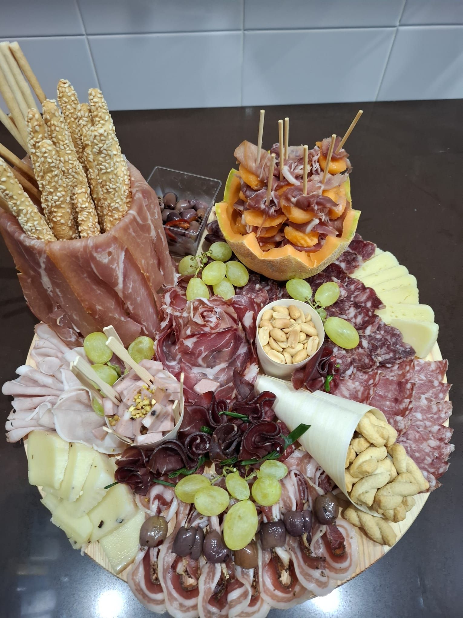 Tagliere di salumi e formaggi, uva, frutta secca, cracker e grissini disposti su un piatto rotondo.