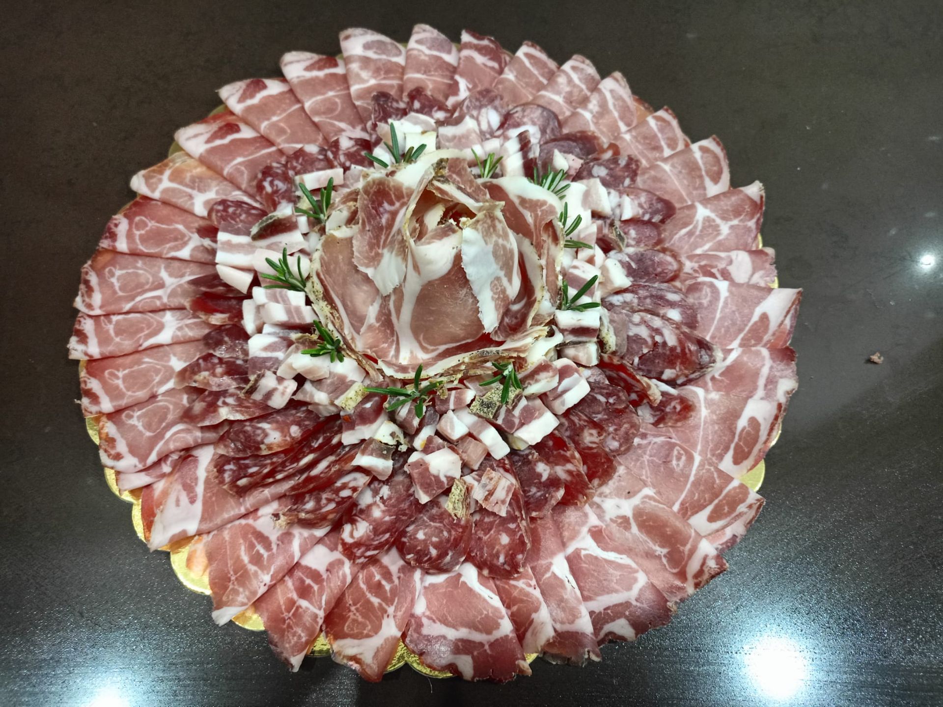 Affettati sottilmente e disposti a formare un fiore su un piatto nero, guarniti con erbe aromatiche.
