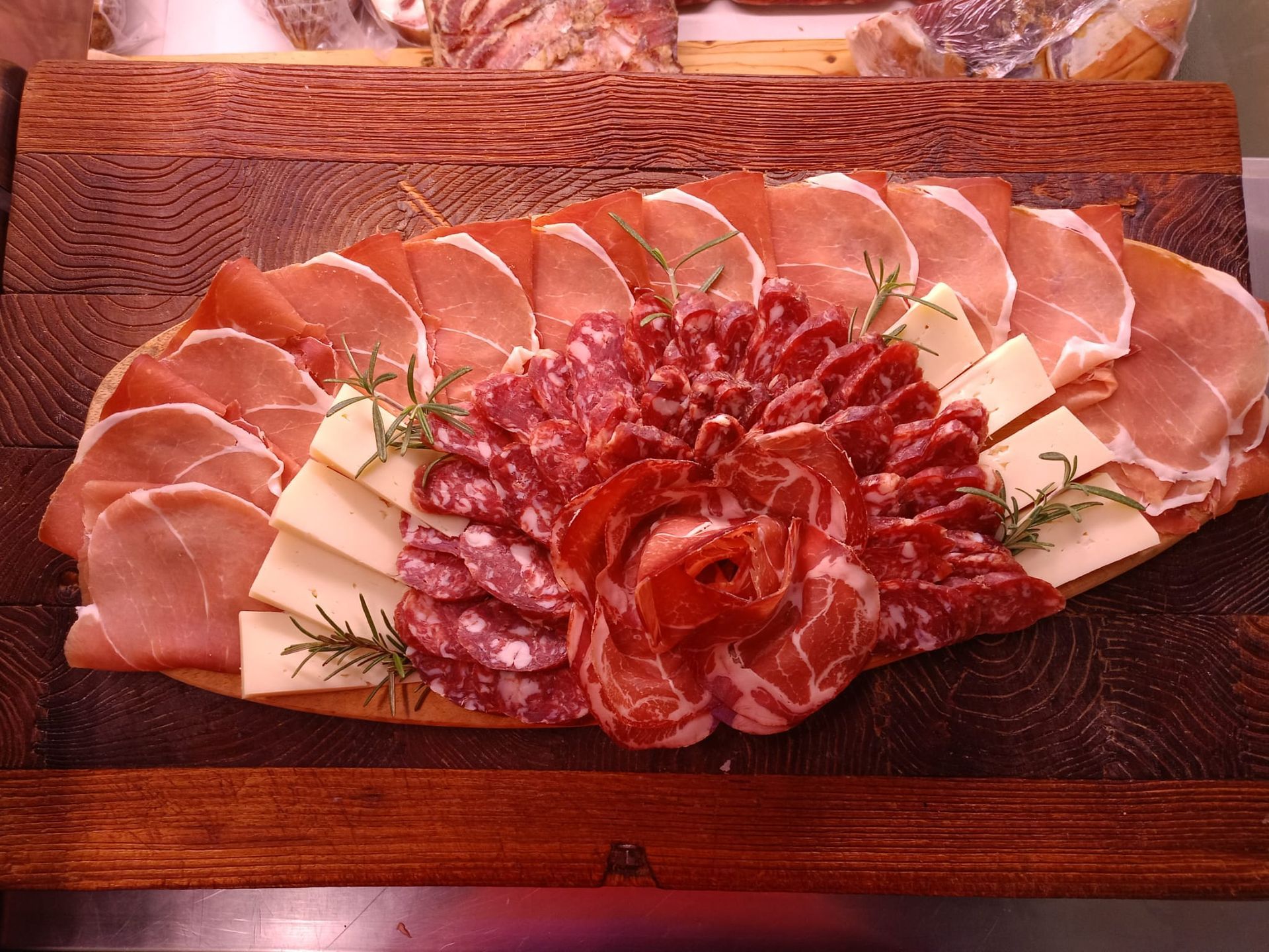 Affettati assortiti di salumi e formaggi disposti su un piatto da portata in legno, guarniti con erbe aromatiche.