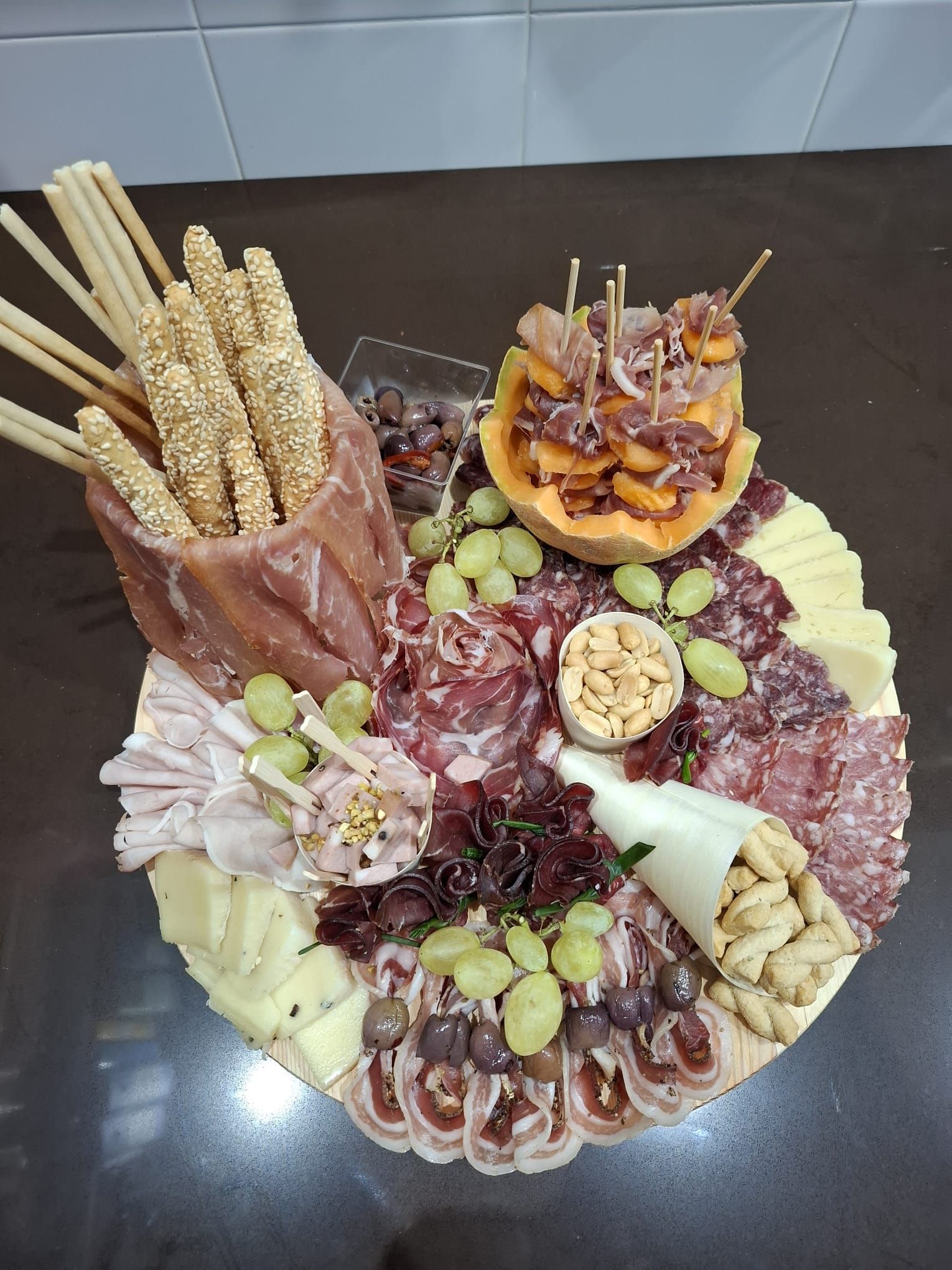 Tagliere di salumi con affettati, formaggi, uva, noci, grissini e frutta secca su un tavolo scuro
