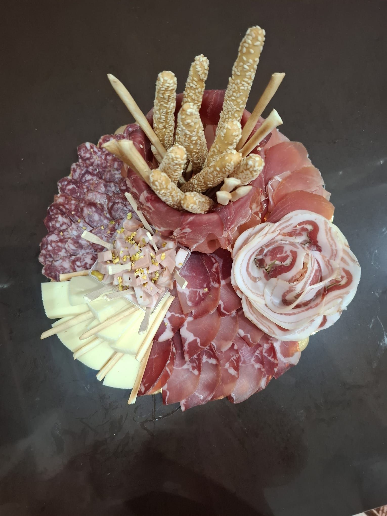Tagliere di salumi con affettati, fette di formaggio, grissini e cracker su un tavolo scuro