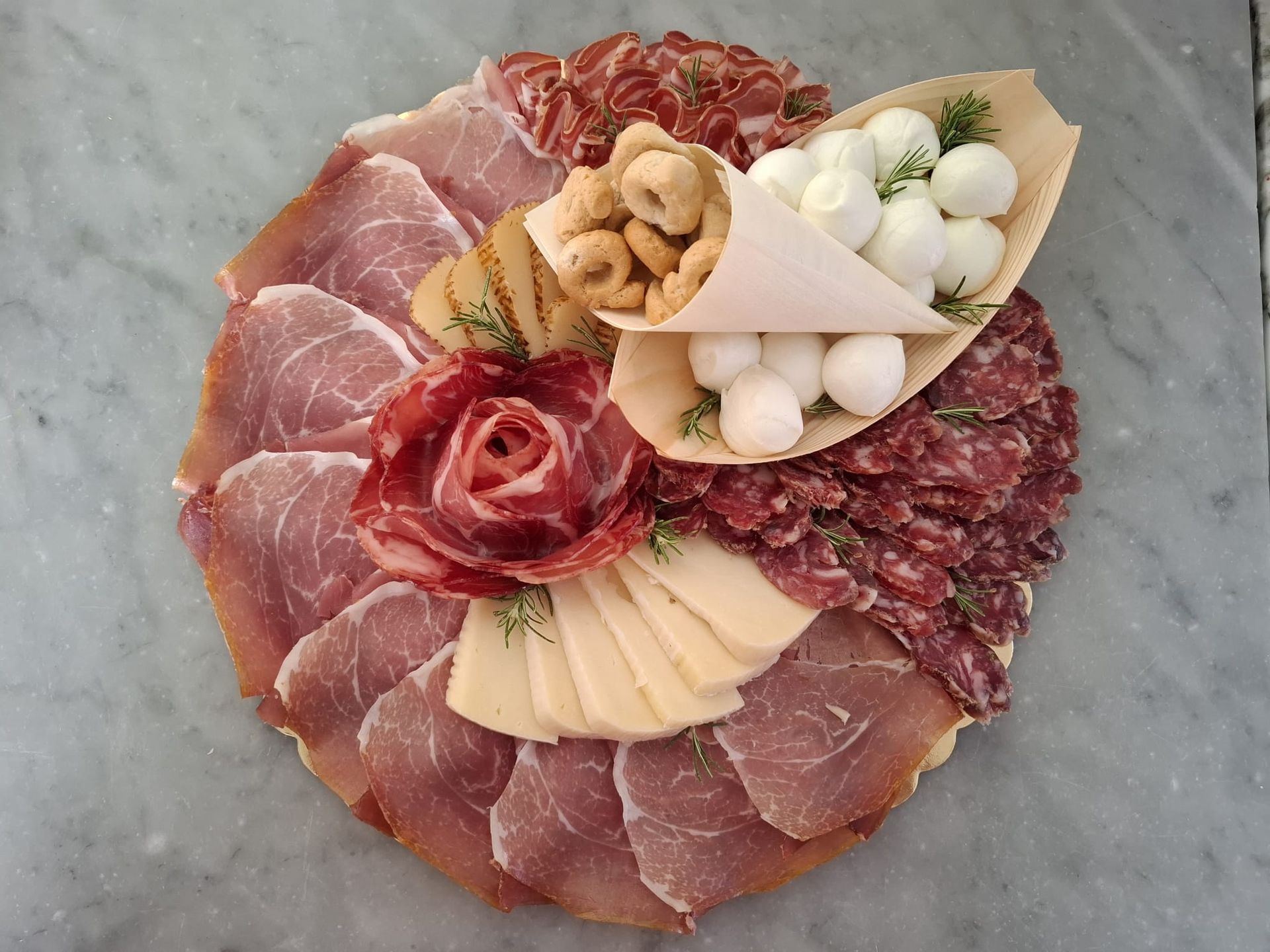 Tagliere di salumi con affettati, formaggi, olive, cracker e guarnizioni disposti a forma di fiore.