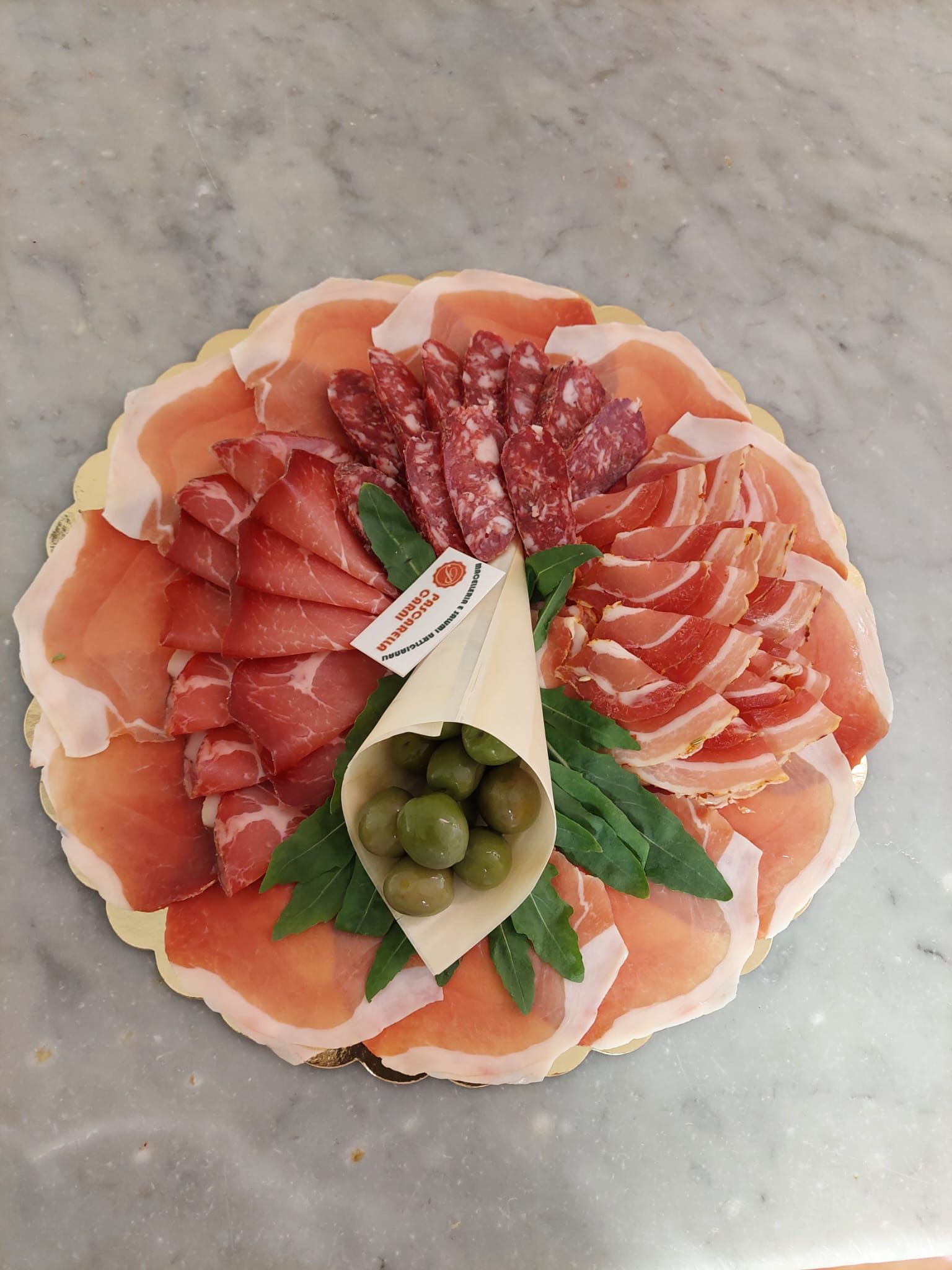 Piatto di salumi con affettati, spicchi di formaggio e olive verdi su una superficie di marmo.