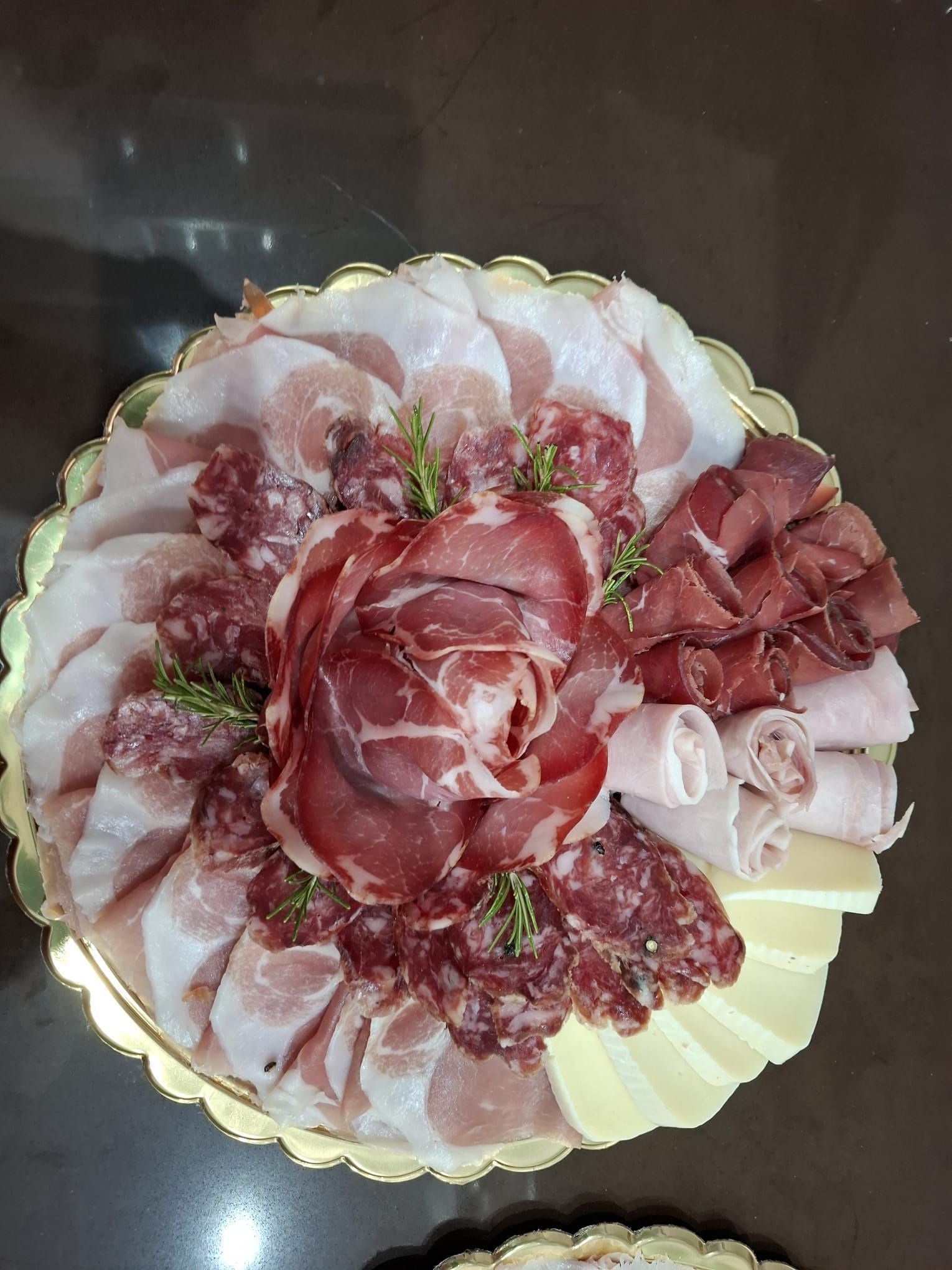 Piatto di salumi assortiti con affettati disposti a rosa su un piatto decorativo.