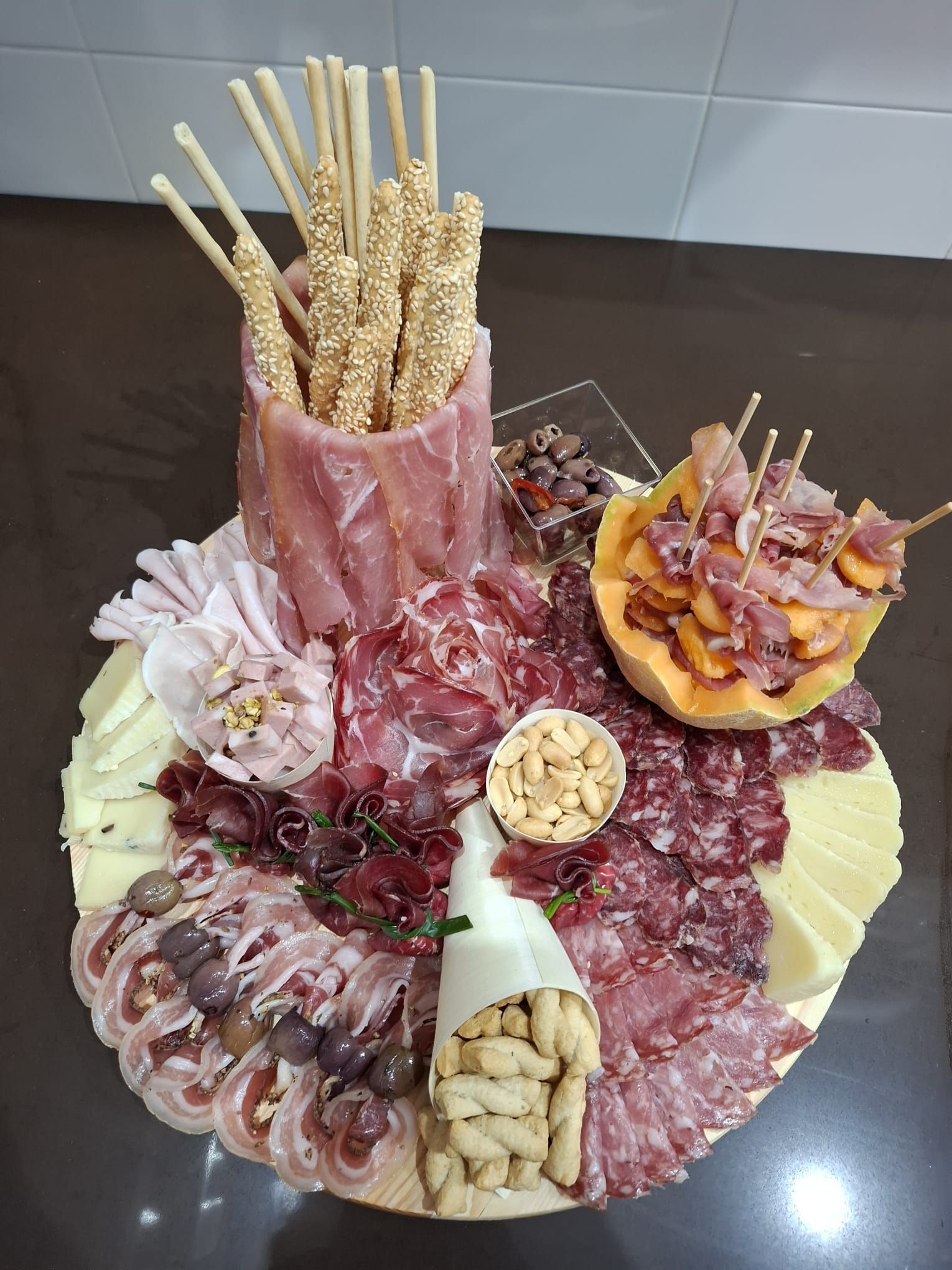 Piatto misto di carne e pesce disposto su un grande piatto bianco, con grissini e guarnizioni.