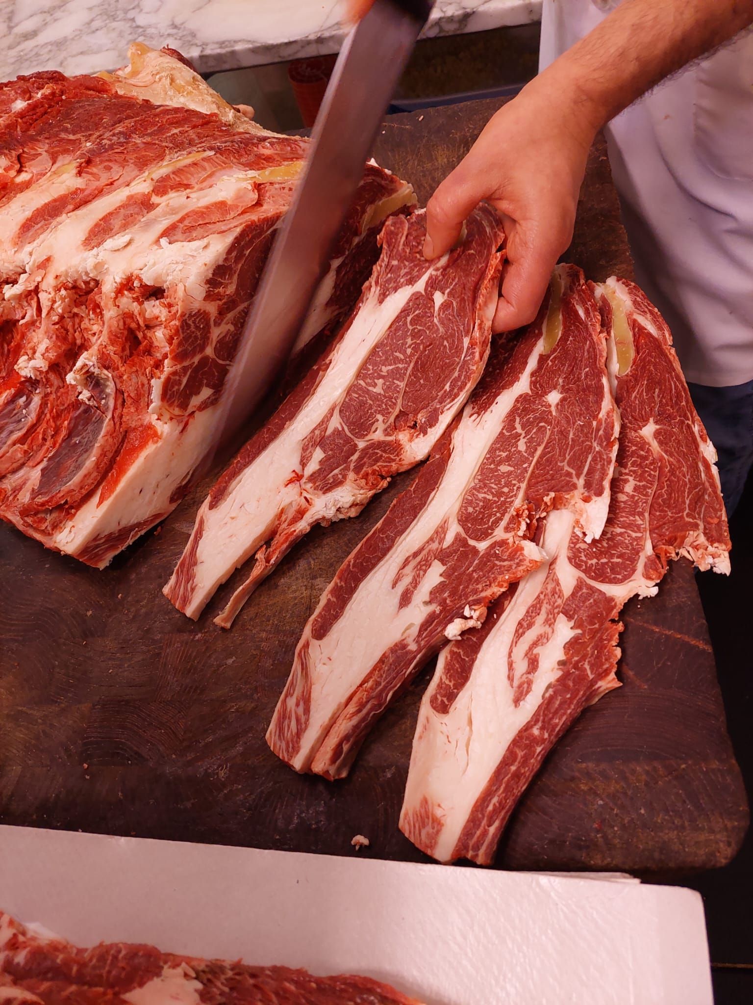 Mani che affettano con un coltello la carne cruda marmorizzata su un tagliere.