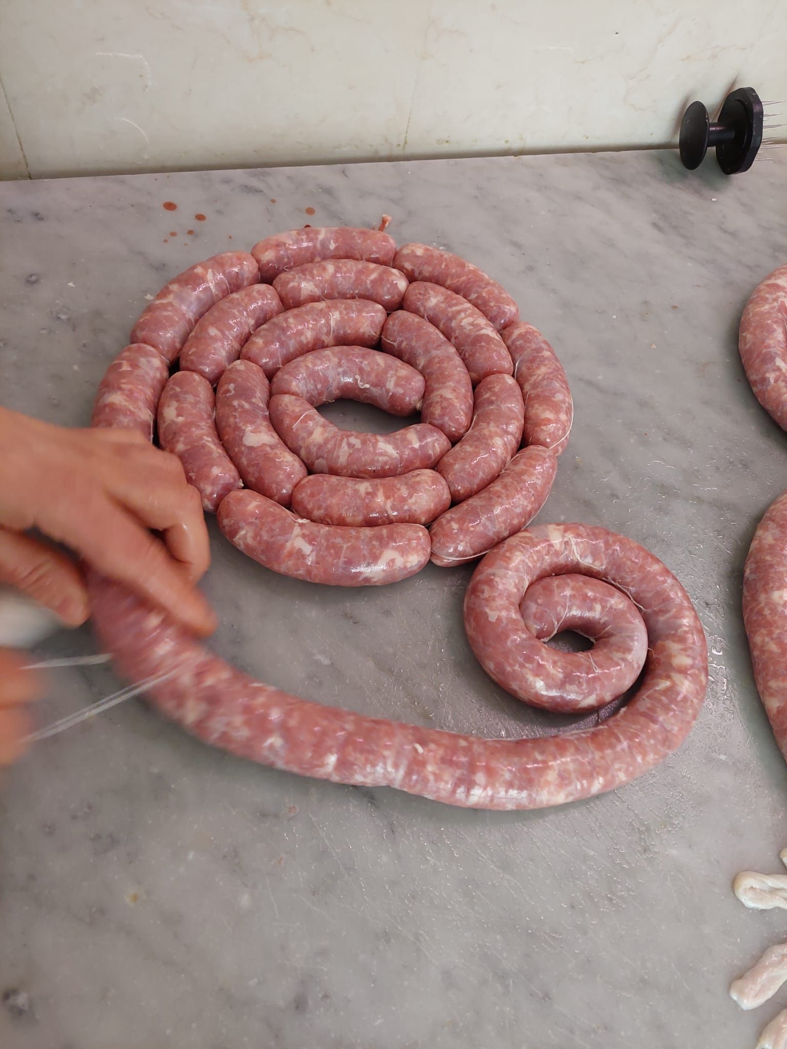 Salsicce crude arrotolate su un pavimento di cemento, con una mano nelle vicinanze.
