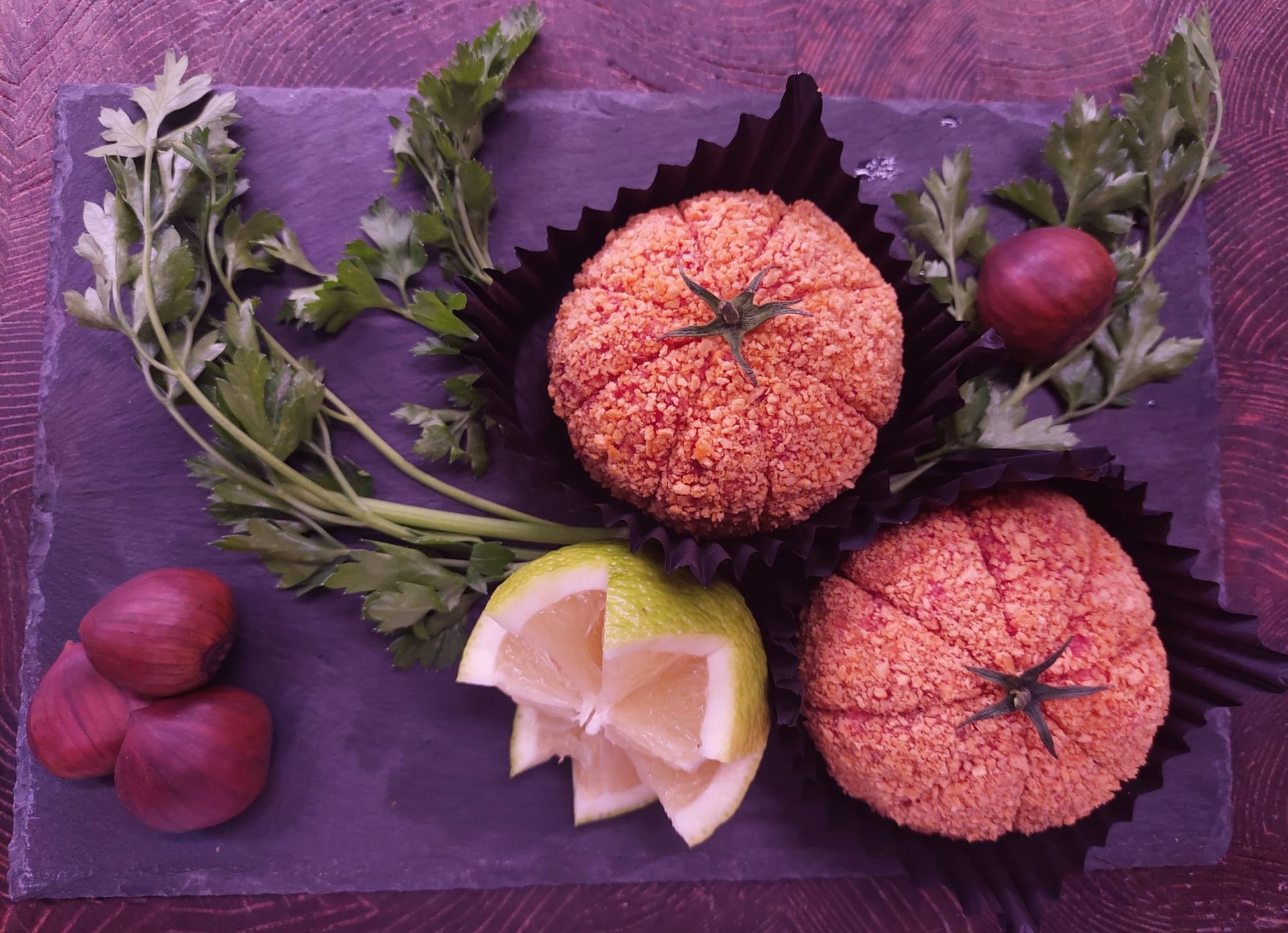 Frutta e foglie assortite disposte su una tovaglia viola con una piccola guarnizione di limone.