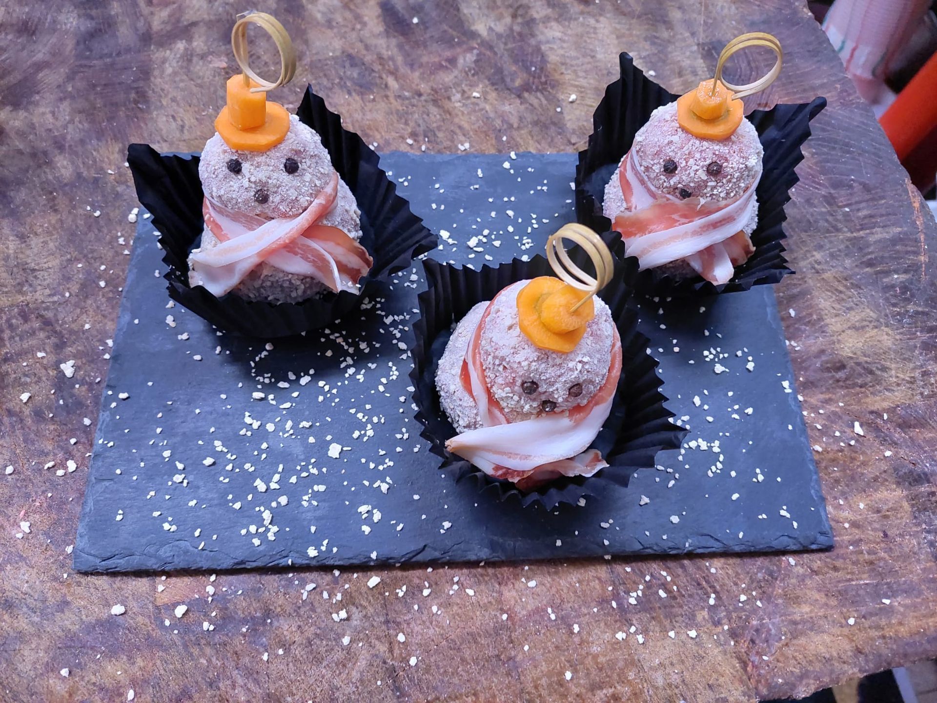 Tre tartine di pesce con guarnizione all'arancia su un tagliere di ardesia nera.