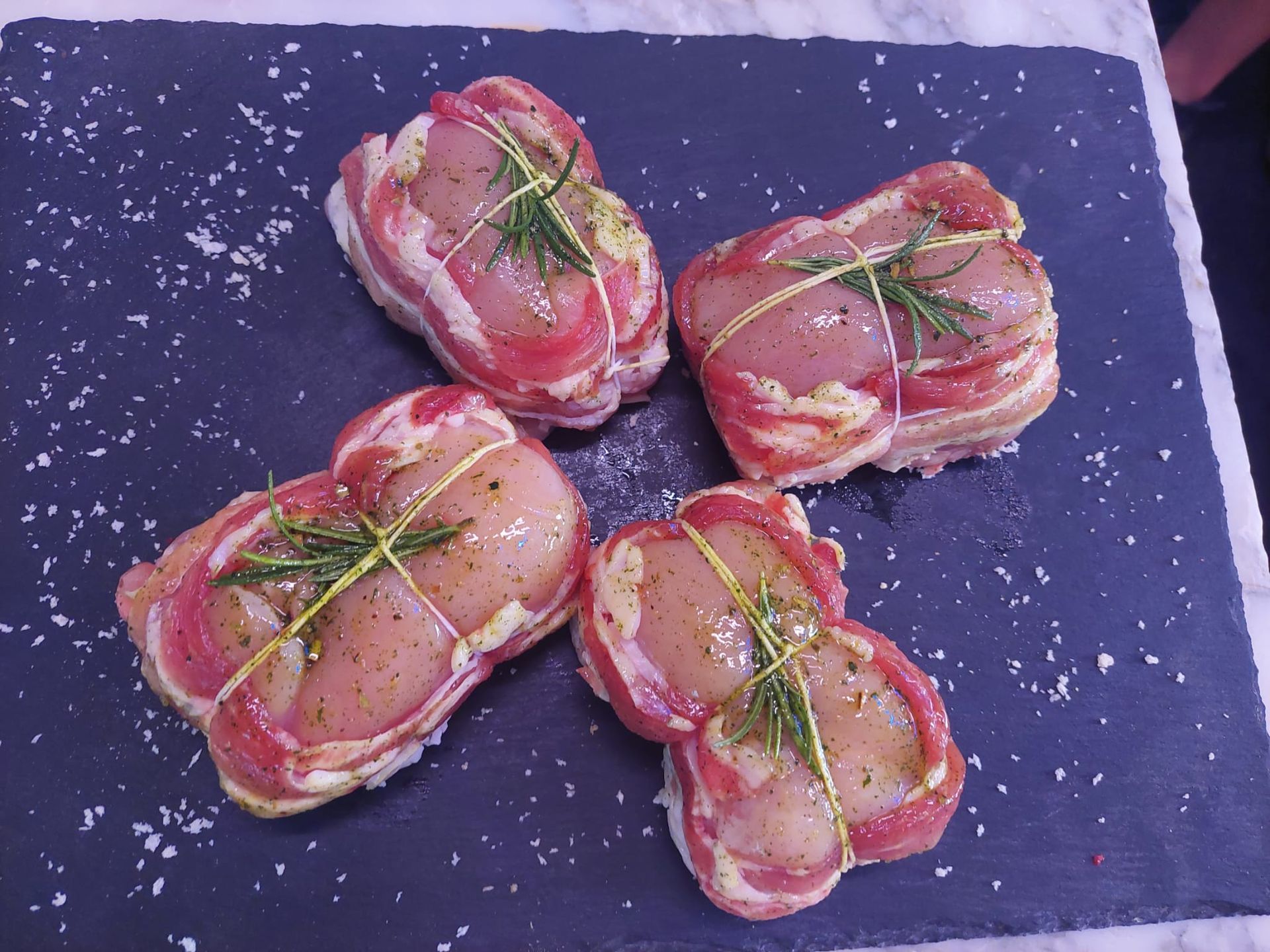 Quattro fagottini di carne cruda legati con erba cipollina su una tavola di ardesia scura, cosparsi di sale