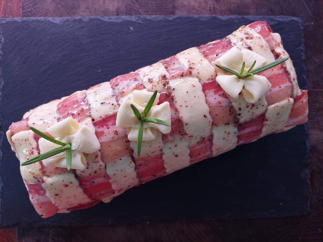 Rotolo da dessert rosso e bianco a fette, guarnito con panna e decorazione verde, servito su un tagliere di ardesia scura.