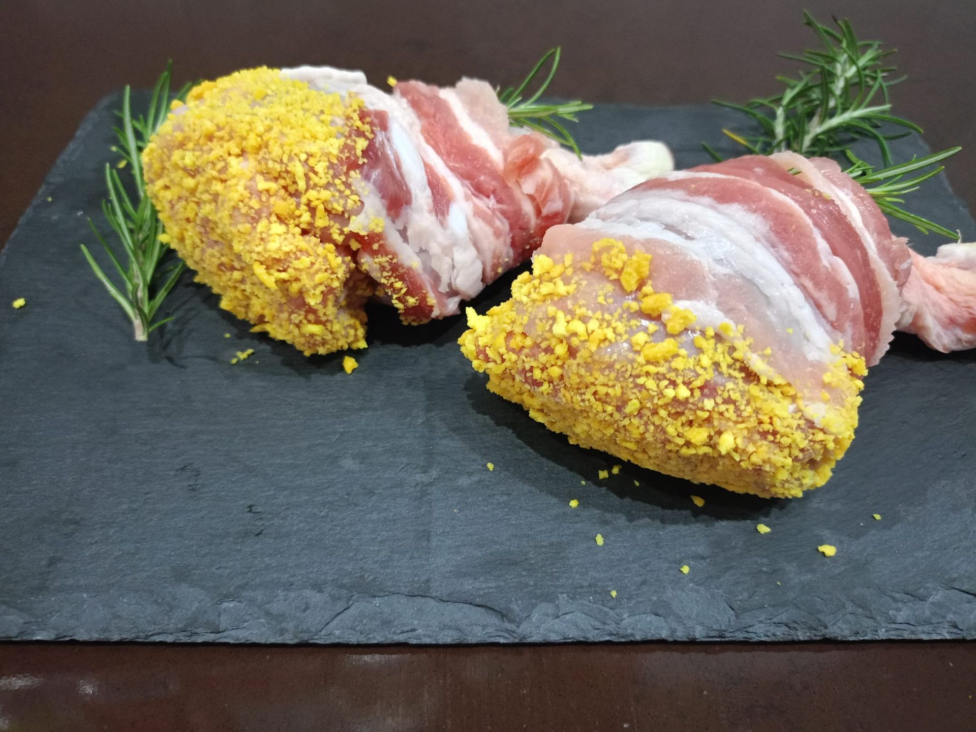 Due involtini di carne cruda in crosta di erbe aromatiche, serviti su un tagliere di ardesia nera e guarniti con rosmarino.