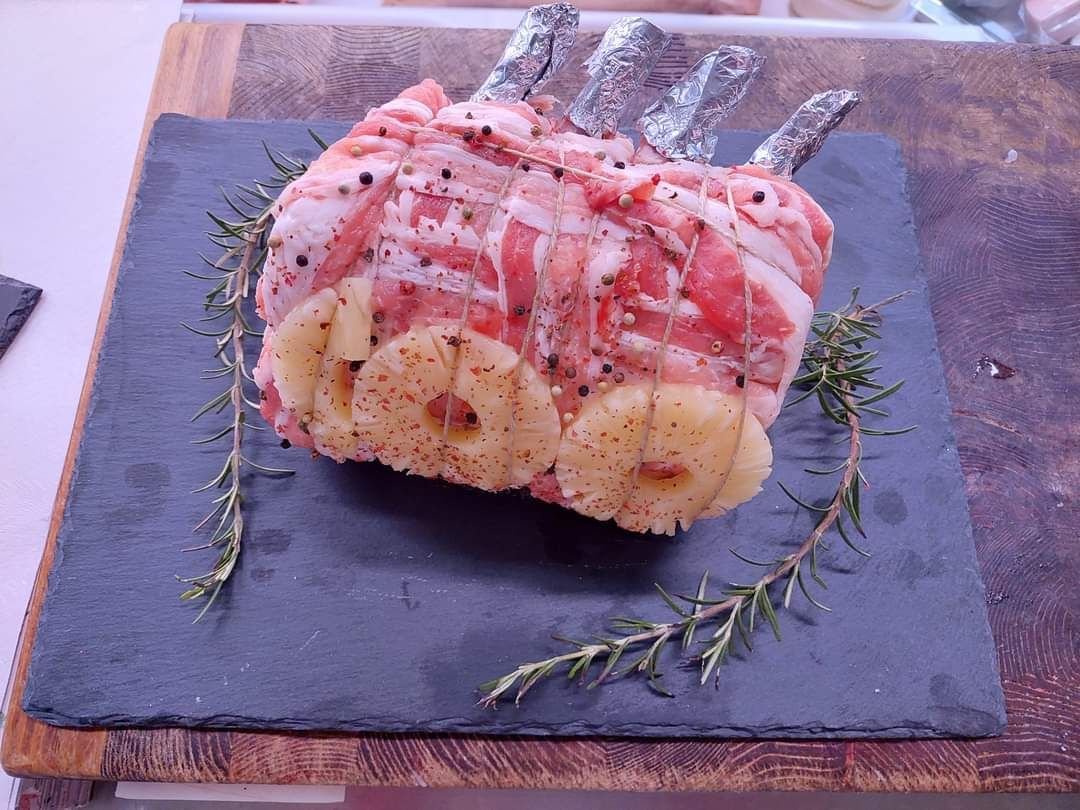 Carne arrosto avvolta in pancetta ed erbe aromatiche, servita su un tagliere di ardesia nera.