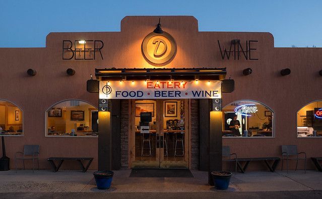 A tan adobe-style restaurant exterior at dusk with a lighted sign above the entrance reading