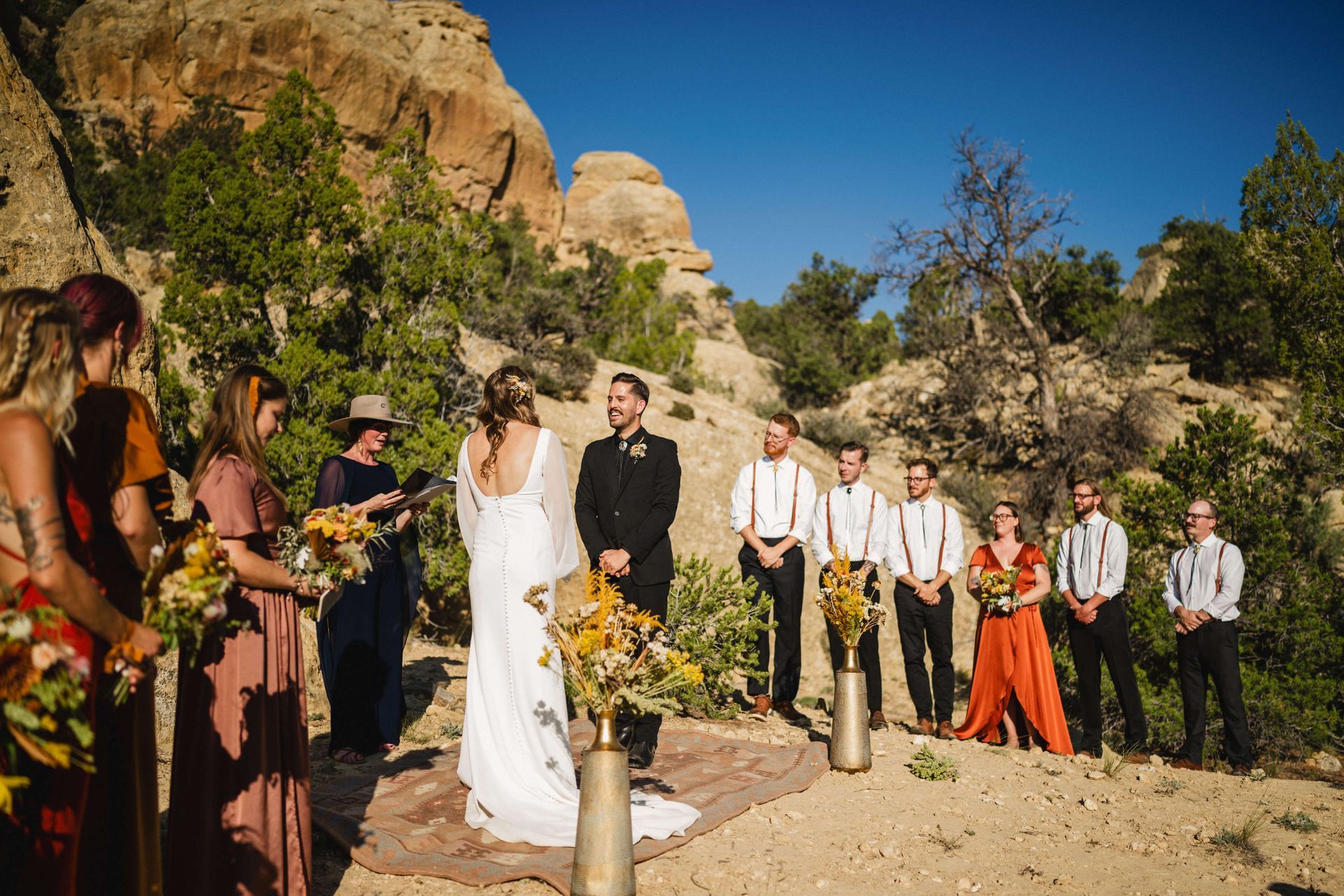 20210905_BrianTessWedding_398 A wedding ceremony outdoors in a rocky, arid landscape, with a couple standing at the altar surrounded by a bridal party.