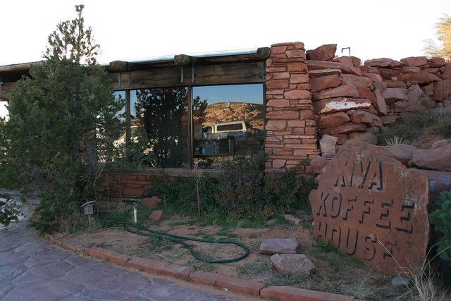 A stone building exterior with a reflection of the surrounding desert landscape and a sign reading