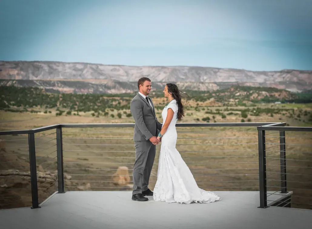 A couple holding hands while facing each other on a deck overlooking a vast, desert landscape.