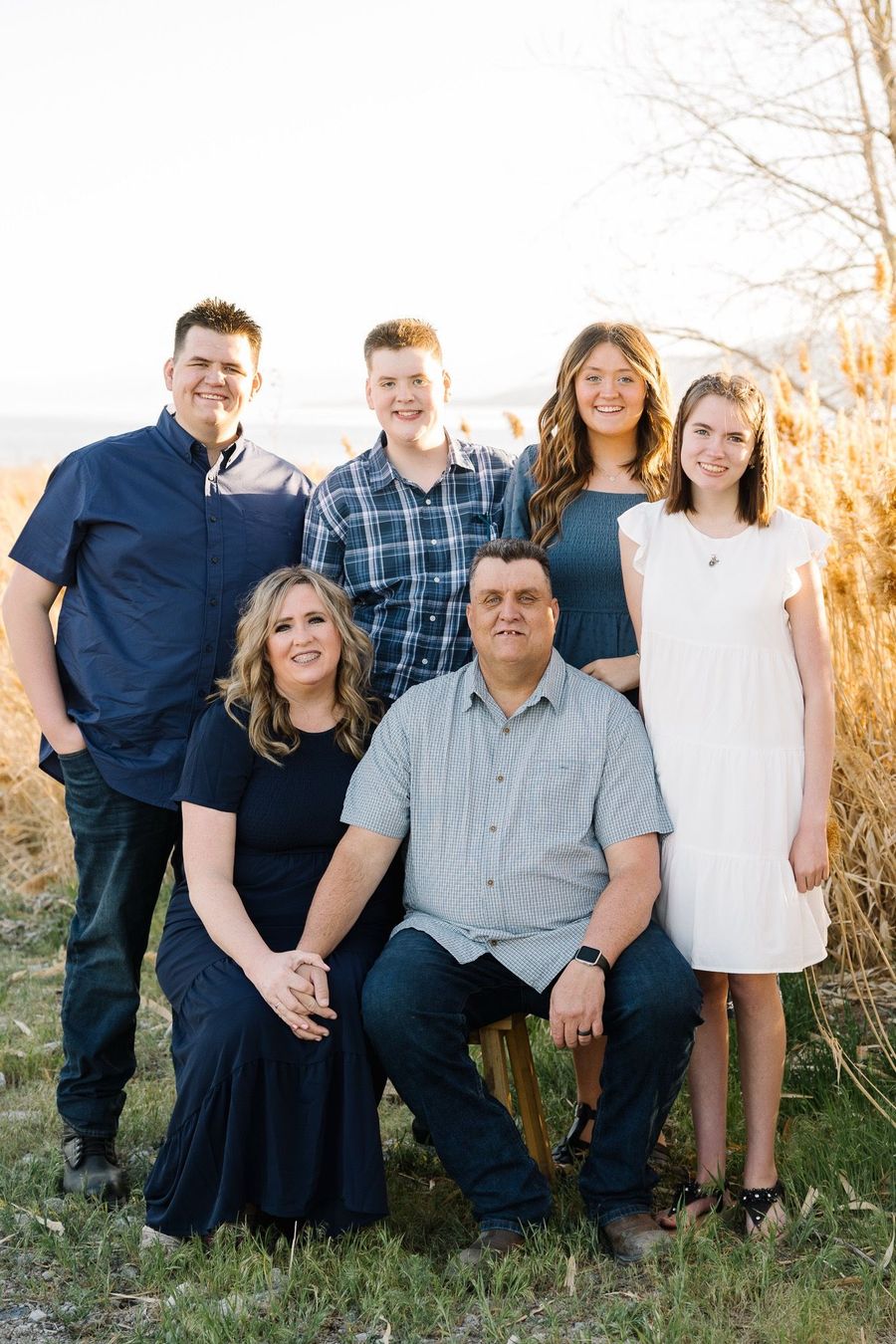 Six people posing outdoors in a garden, with tall grass and warm sunlight.