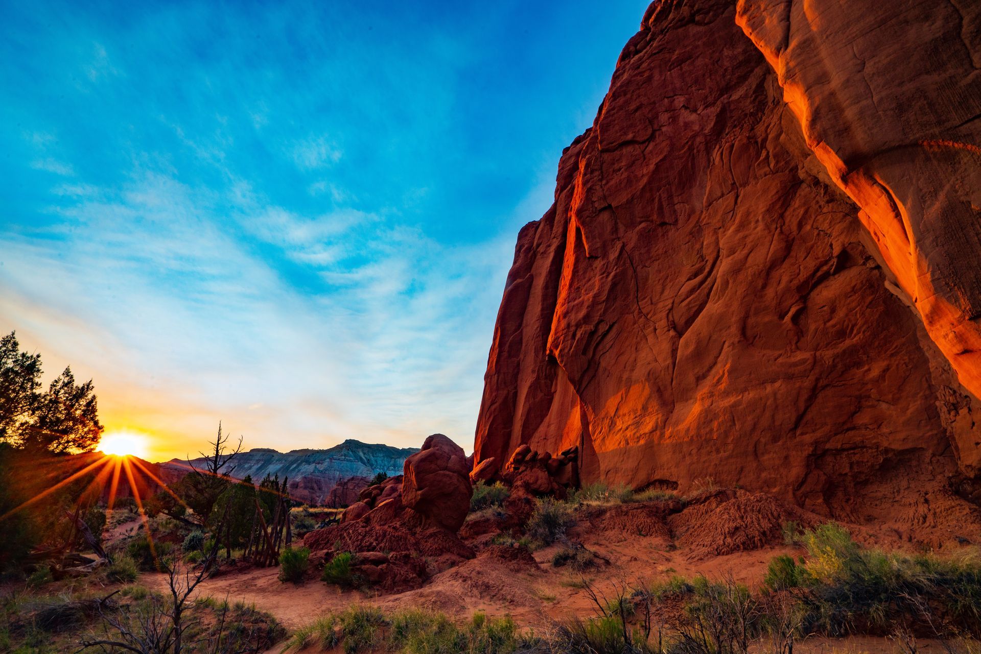 Sunset over red sandstone cliffs with desert brush and a blue sky