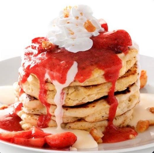 A round fried pastry on a red plate, topped with strawberry jam, green fruit compote, whipped cream, and chopped walnuts.