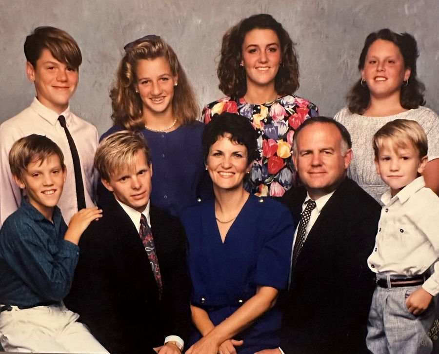 Family portrait of seven people posed in two rows, dressed in formal clothing against a studio backdrop