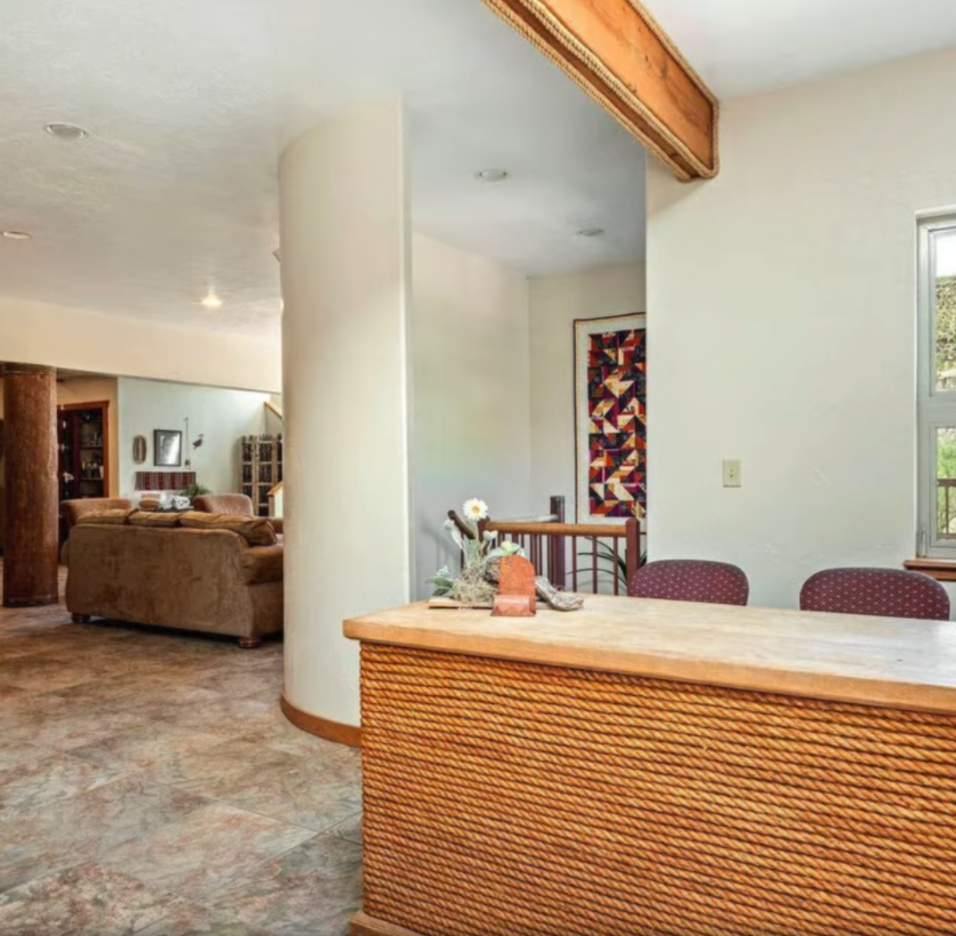 A room with a textured, rope-wrapped counter in the foreground, leading to a curved wall and a view of a living area.