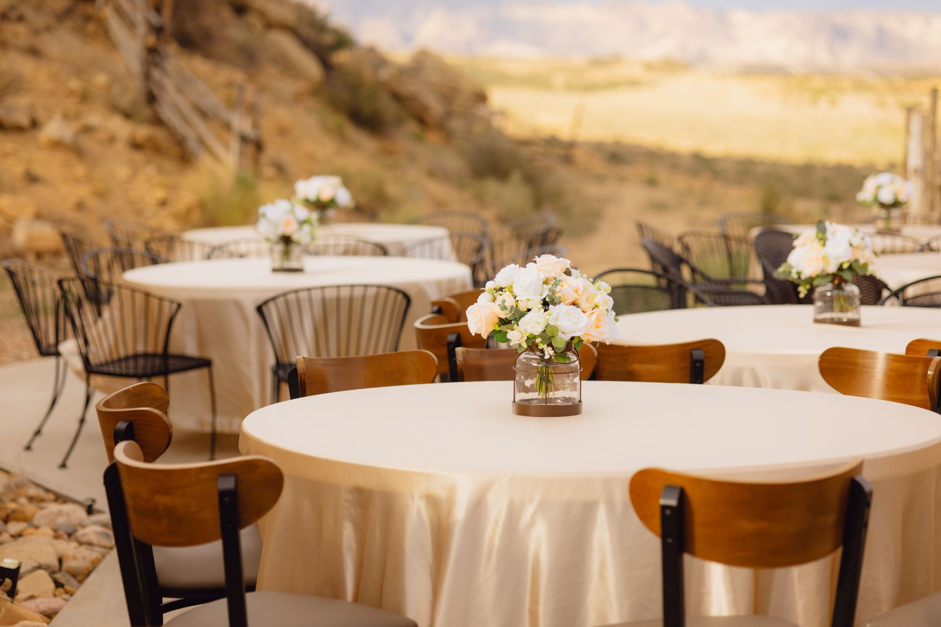 Round dining tables with white tablecloths and floral centerpieces set up outdoors against a desert landscape.