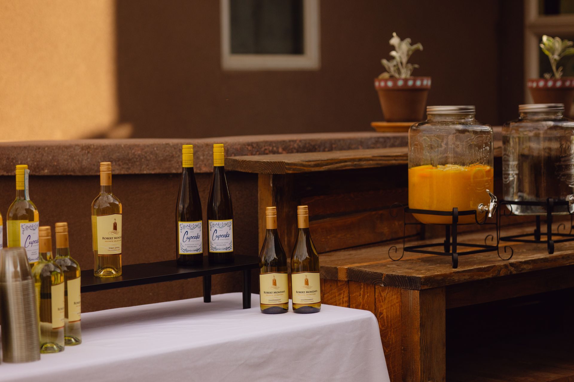 A table set up with several wine bottles and two large drink dispensers filled with orange liquid on a patio.