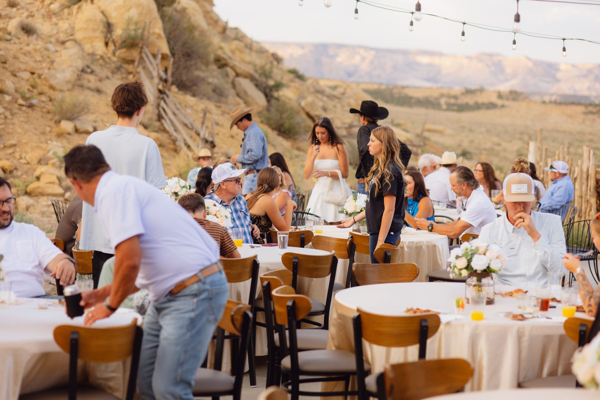 Outdoor reception with round tables and chairs at a desert venue with rocky hills in the background.