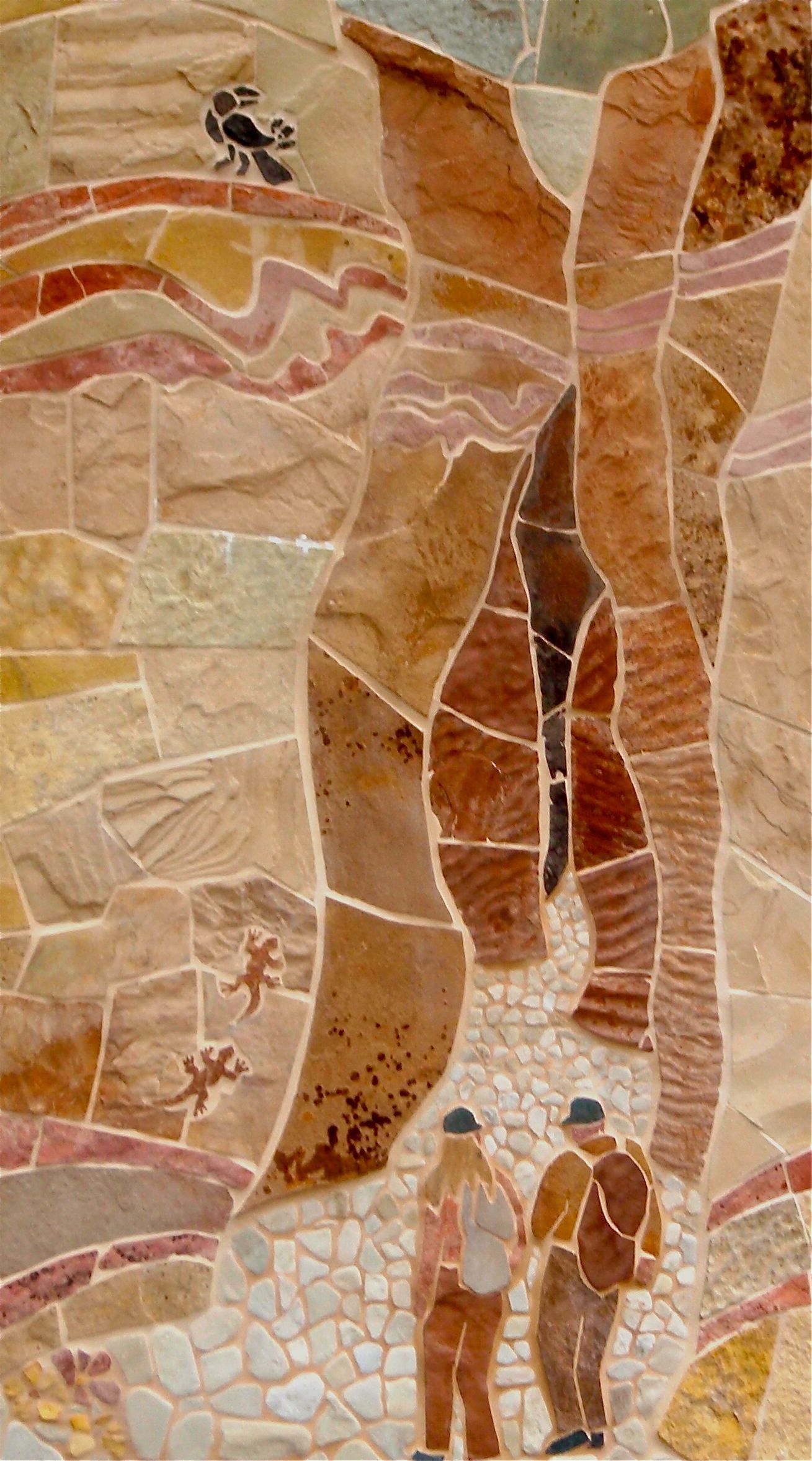 OLYMPUS DIGITAL CAMERA A stone mosaic mural showing two hikers walking through a desert canyon, featuring geological layers and small wildlife.