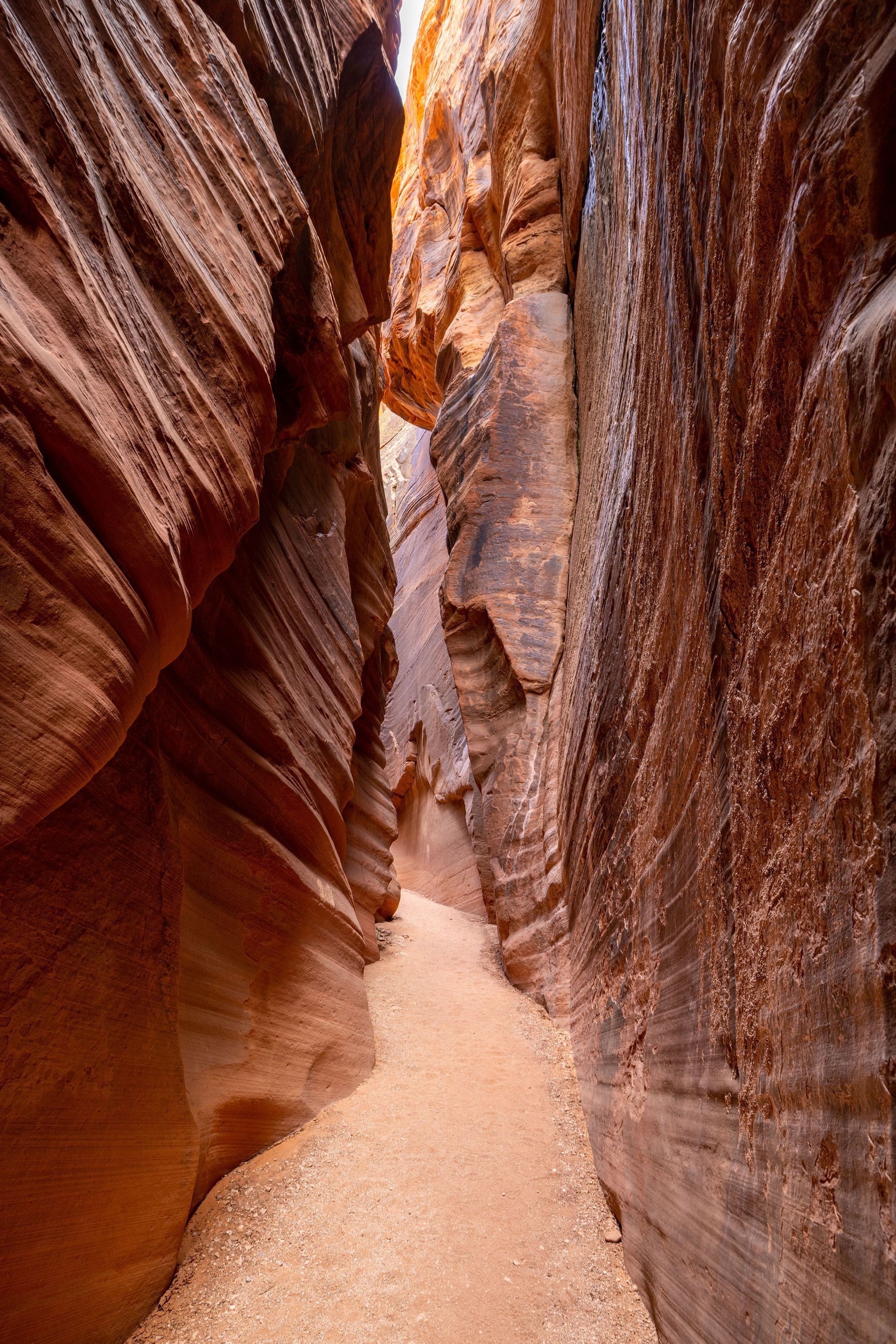 Narrow sandstone canyon with a sandy path and warm red-orange rock walls