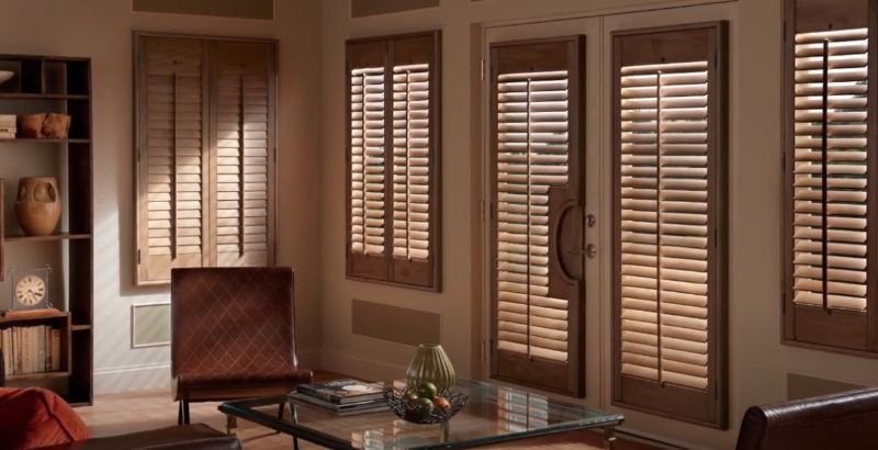 A living room with a couch , chair , table and shutters on the windows.