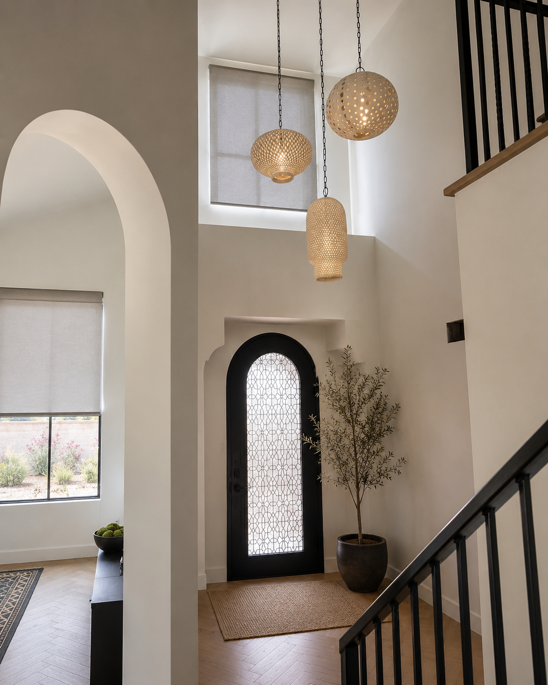 Bright entryway with arched doorway, hanging pendant lights, black staircase railing, and potted plant