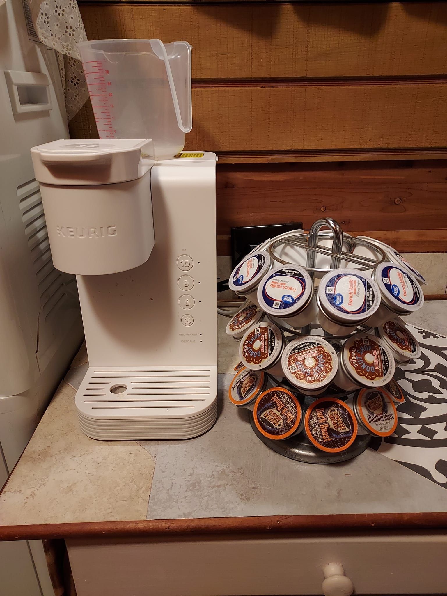 White coffee maker and K-cup carousel on a counter. The coffee maker has a water reservoir.