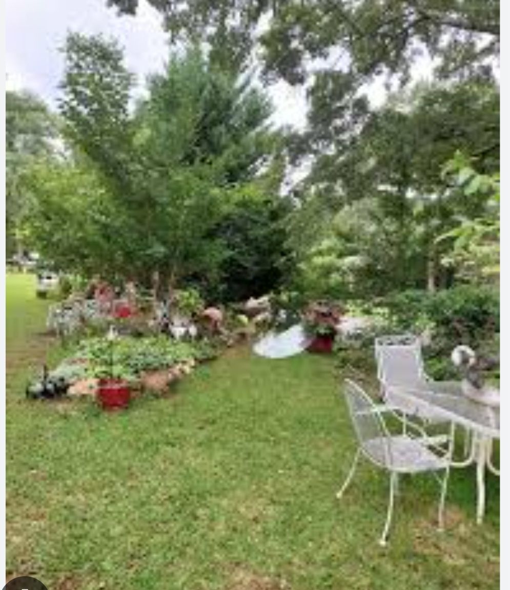 A grassy backyard with a white patio set and colorful flower pots alongside a flowerbed.