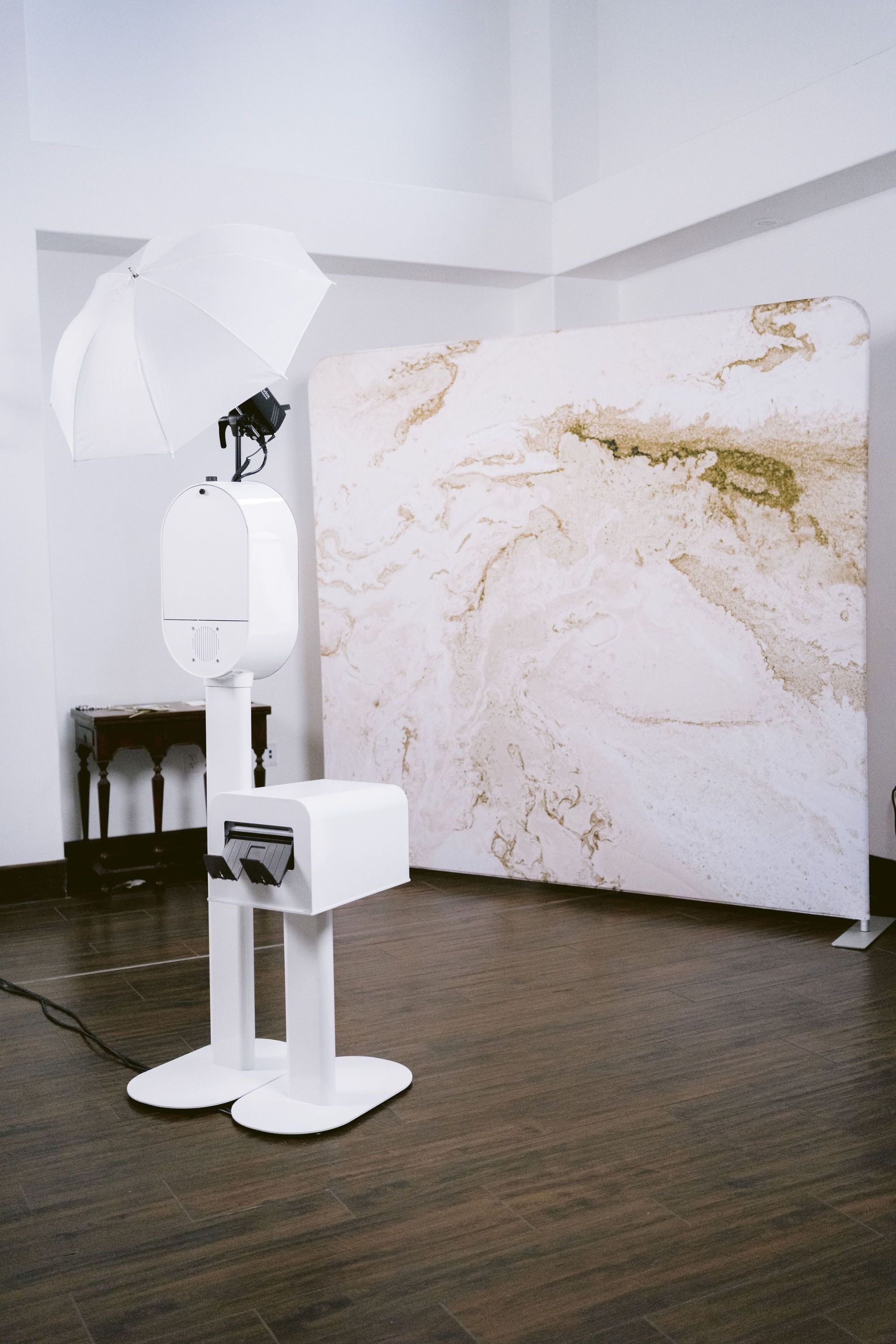 The white Be You Luxe Booth with umbrella light, printer stand, and marble backdrop set up in a venue