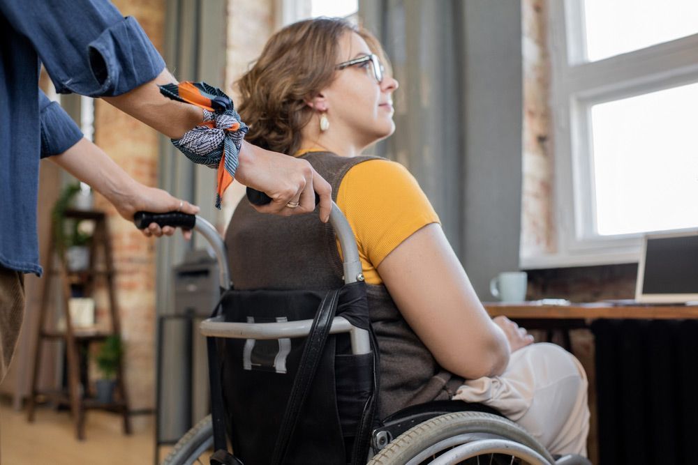 A Woman In A Wheelchair Is Being Helped By A Man — NQ Health In Bayview Heights, QLD