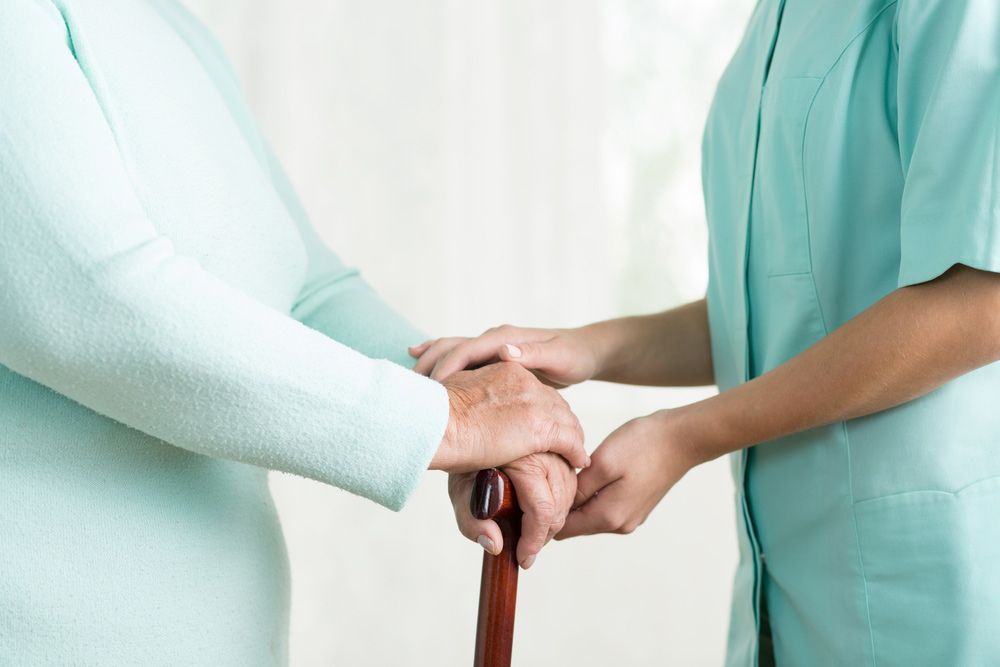 A Nurse Is Holding The Hand Of An Elderly Woman Holding A Cane — NQ Health In Bayview Heights, QLD