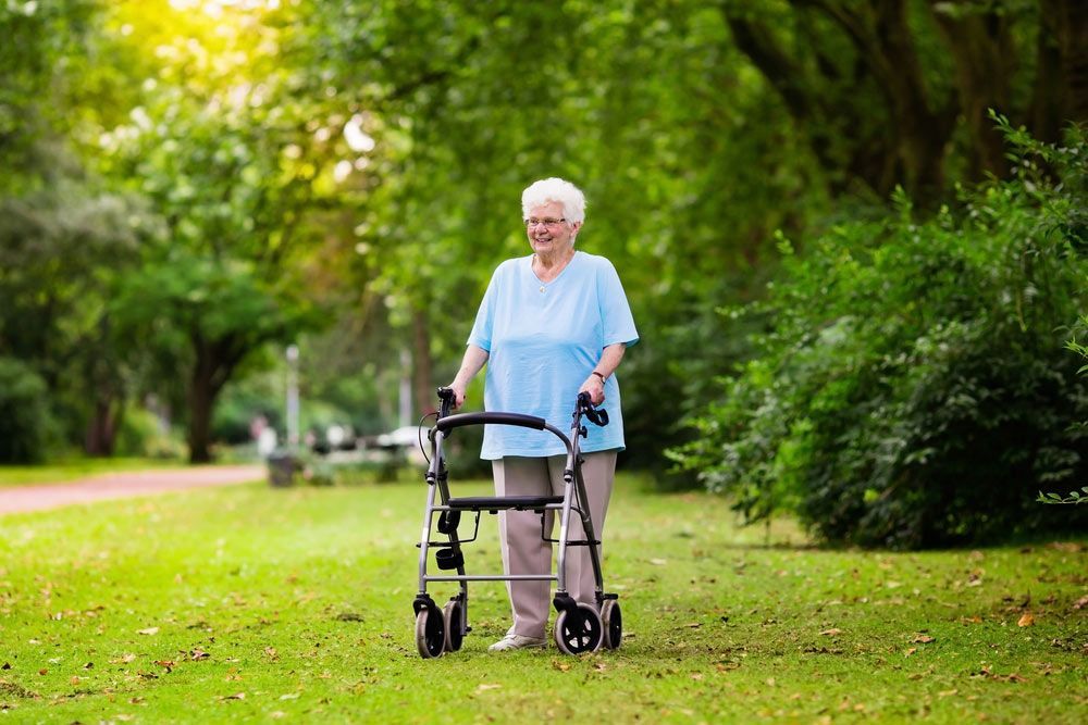 An Elderly Woman Is Walking With A Walker In A Park — NQ Health In Bayview Heights, QLD