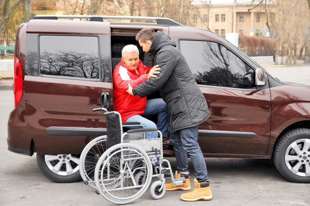 A Man Is Helping An Elderly Woman In A Wheelchair Into A Van — NQ Health In Bayview Heights, QLD