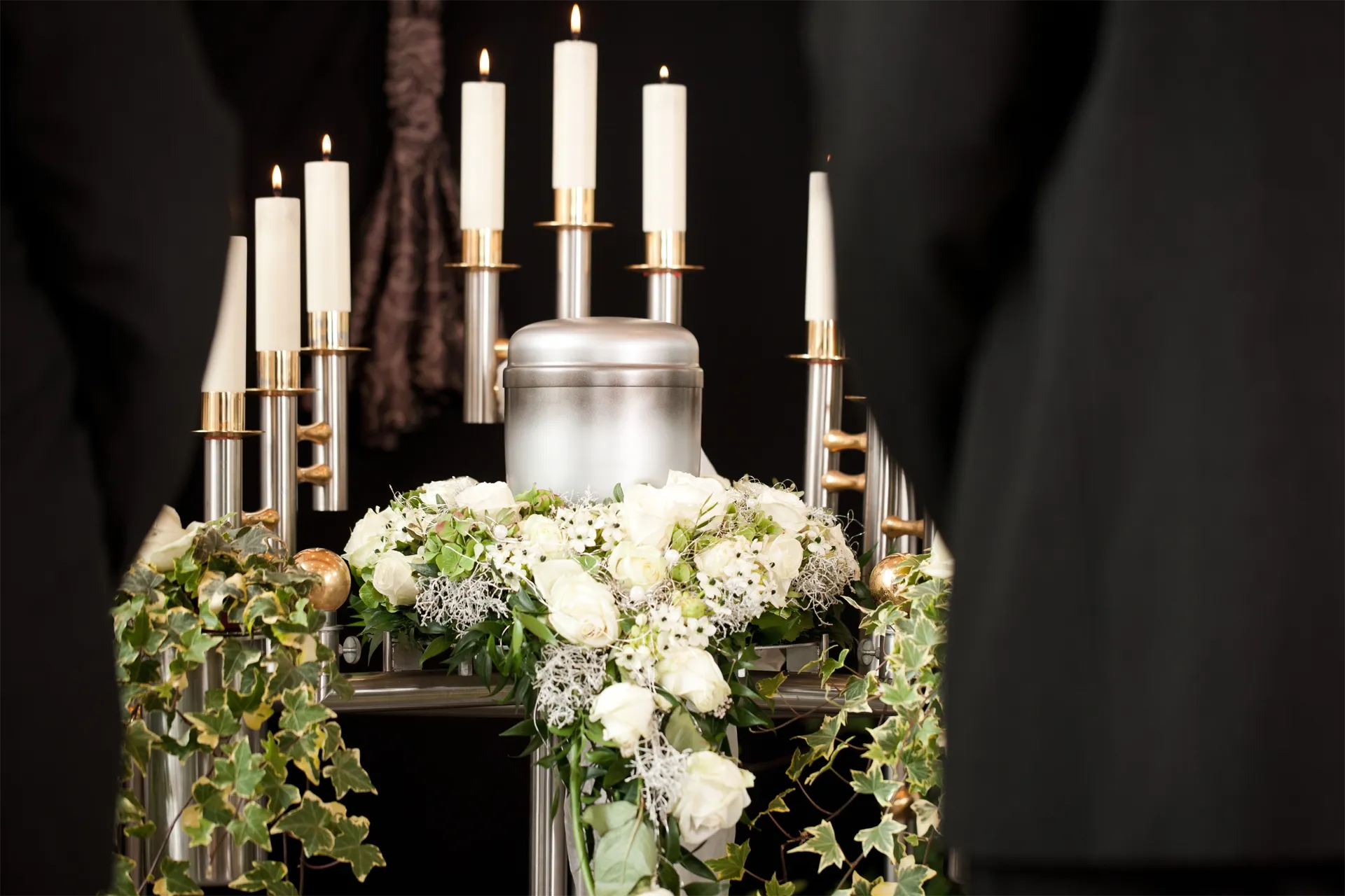 White floral funeral arrangement with candles and greenery on a dark background