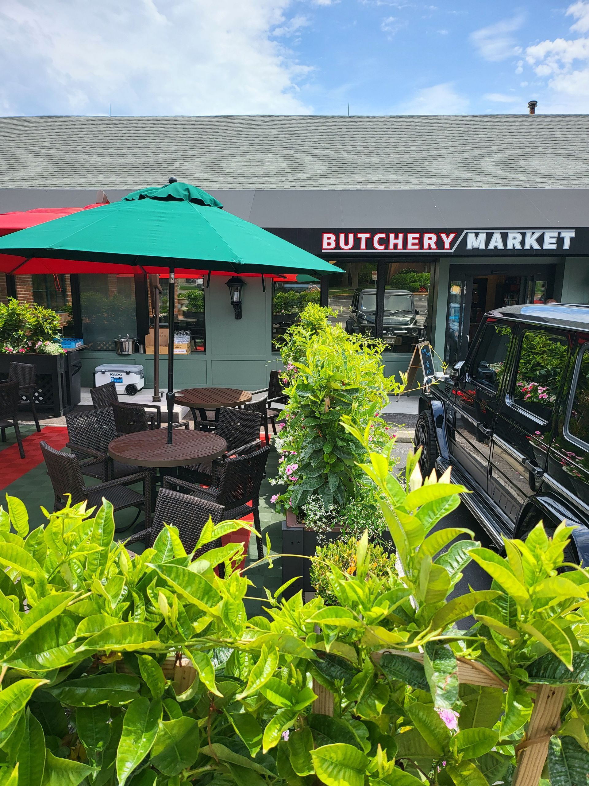 A butchery market with tables and chairs and umbrellas in front of it.