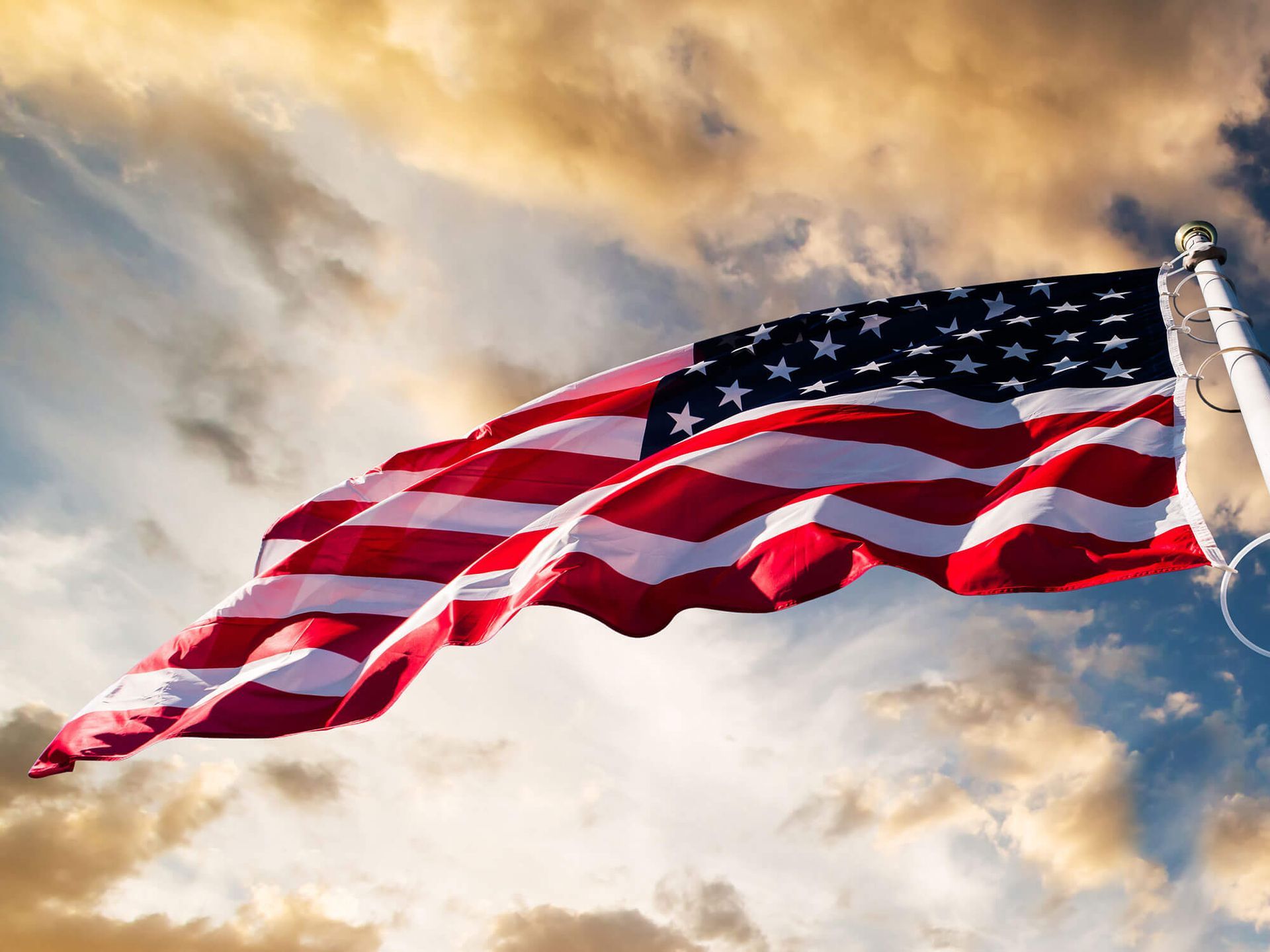 An american flag is waving in the wind against a cloudy sky.